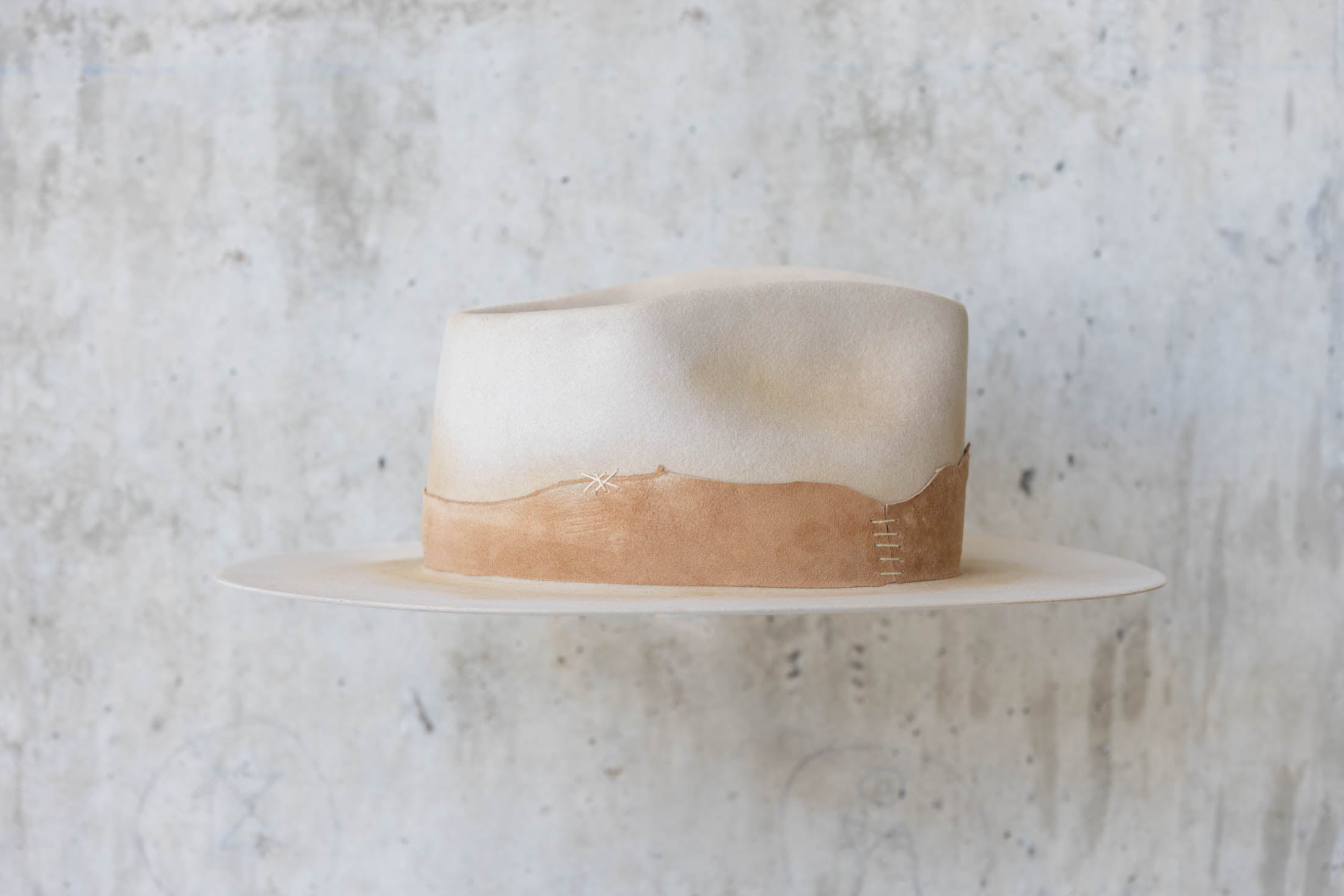 A beige Western hat with a teardrop crown and brown leather band right side