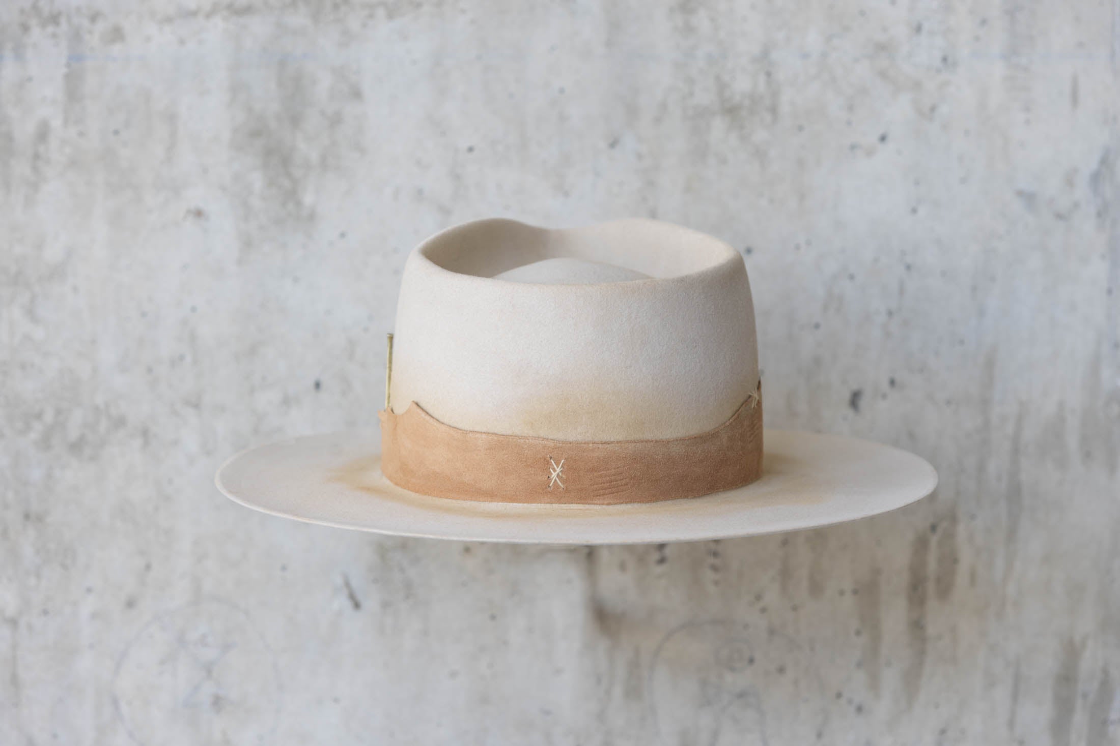 A beige Western hat with a teardrop crown and brown leather band back