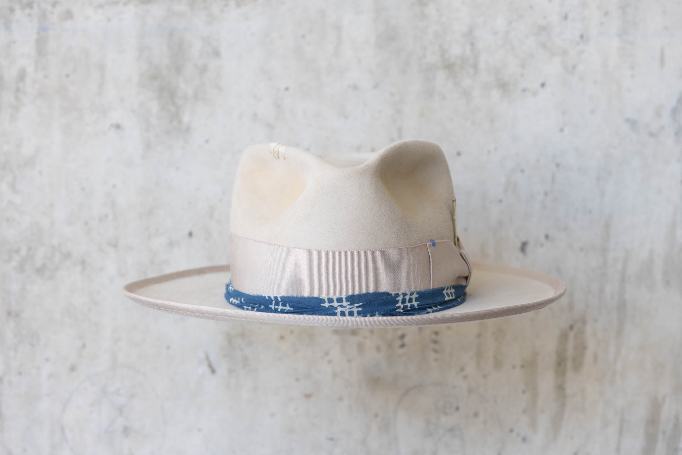 A beige fur hat with a teardrop crown, beige and blue band front side
