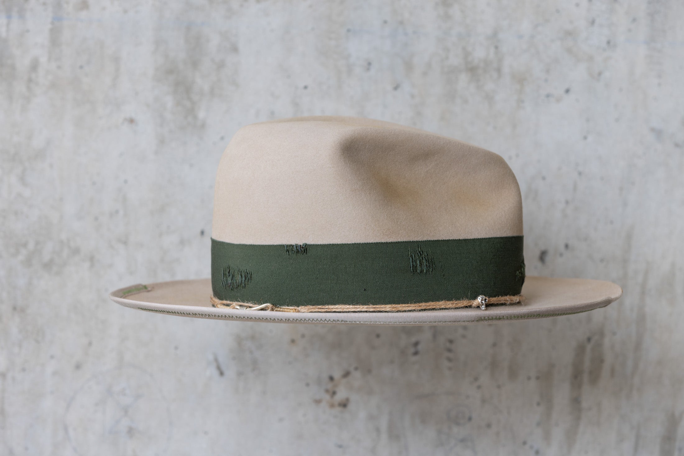 A beige cowboy hat with a forest green grosgrain band and a silver nail on the side right side
