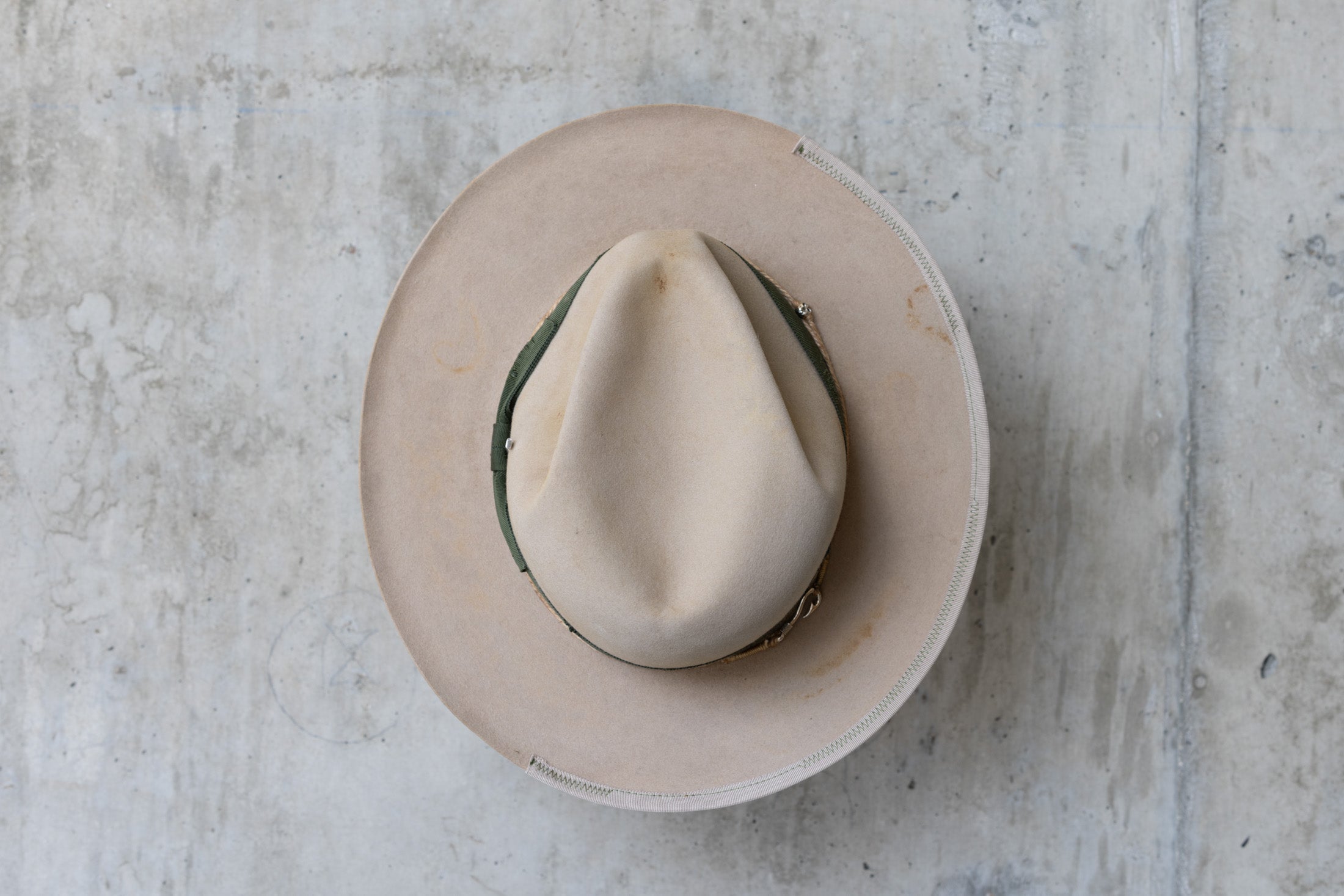 A beige cowboy hat with a forest green grosgrain band and a silver nail on the side top