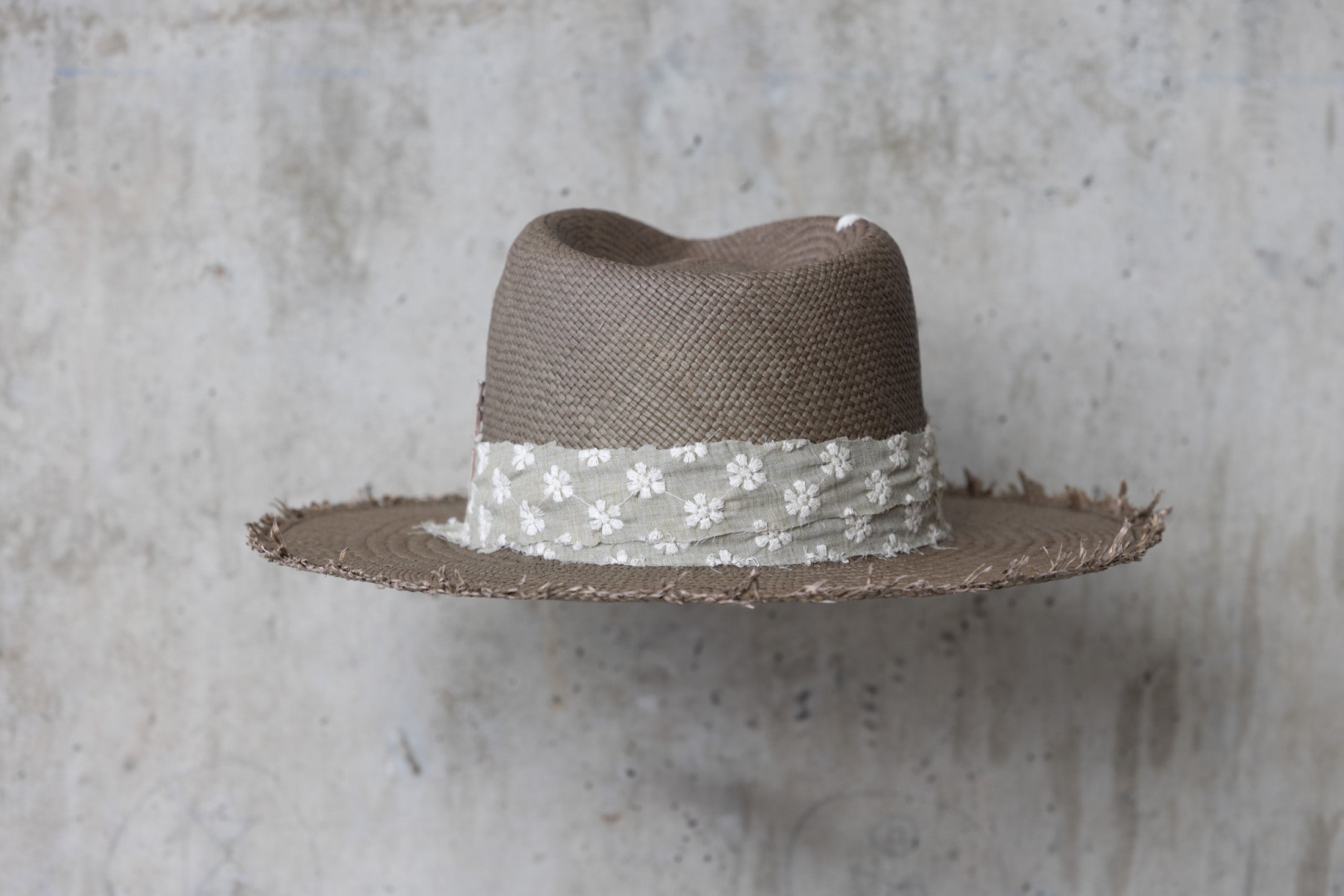 A sage green straw hat with a teardrop crown and linen band with stitched flowers back
