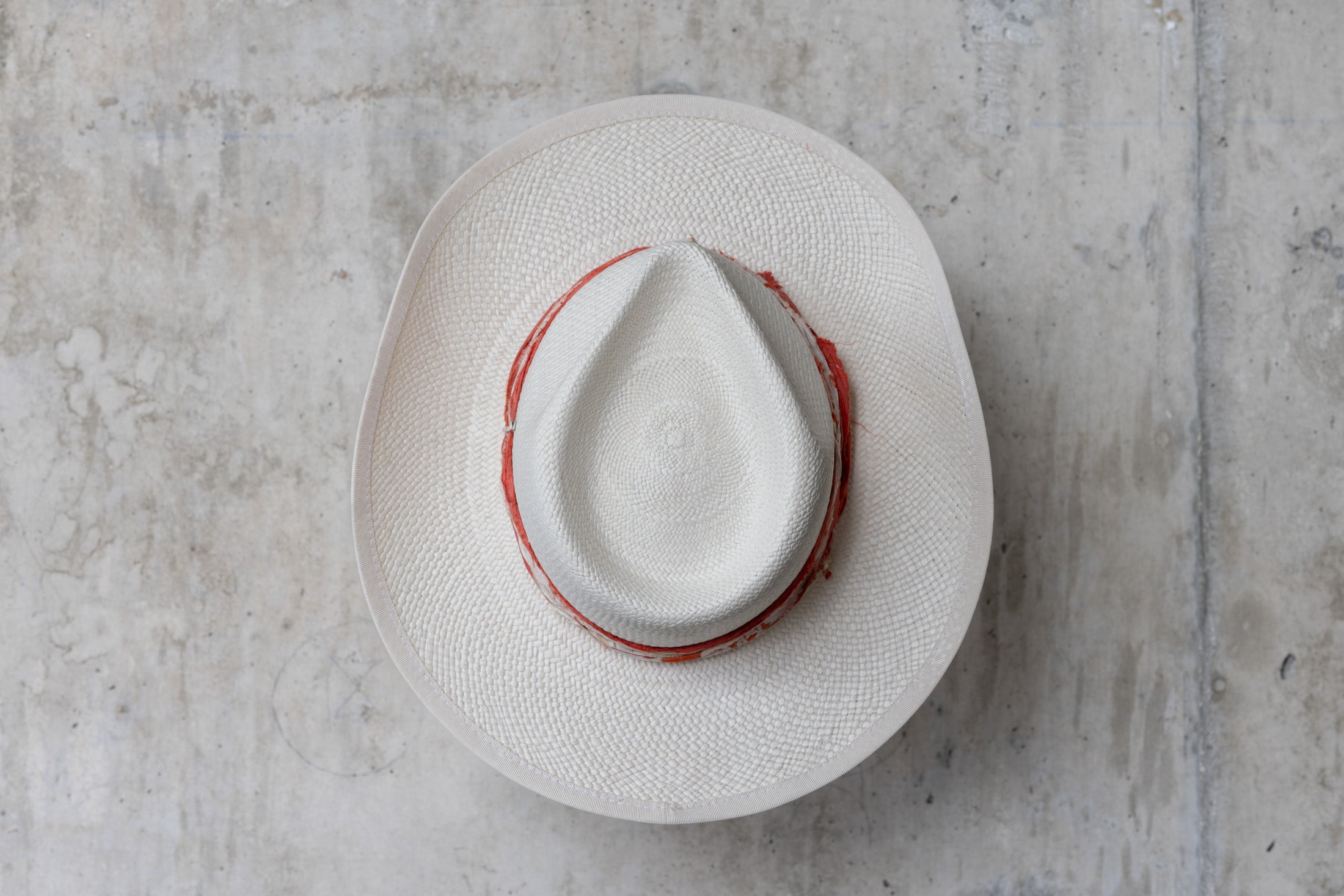 A white straw hat with an orange and cream band and a teardrop crown top