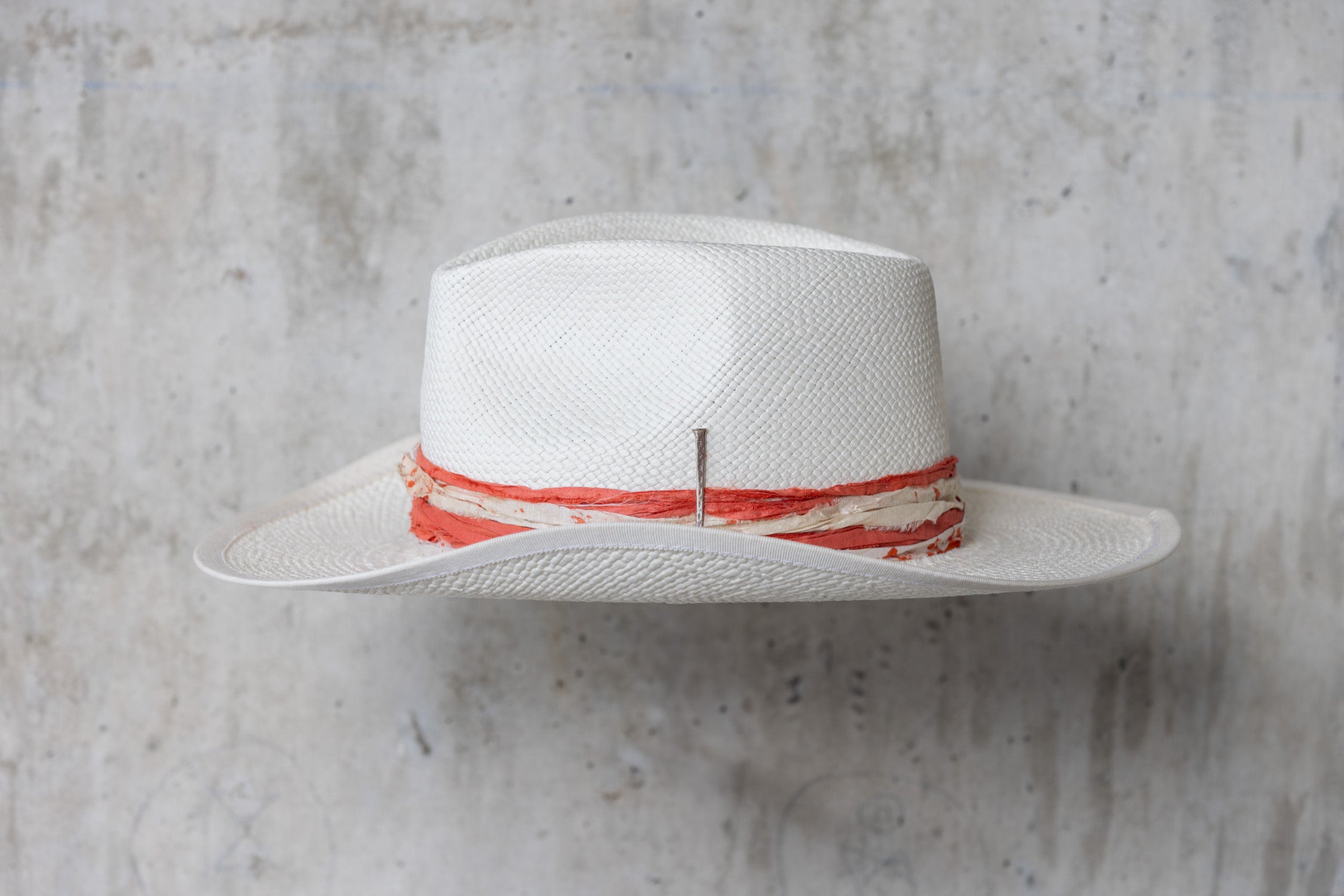 A white straw hat with an orange and cream band and a teardrop crown left side