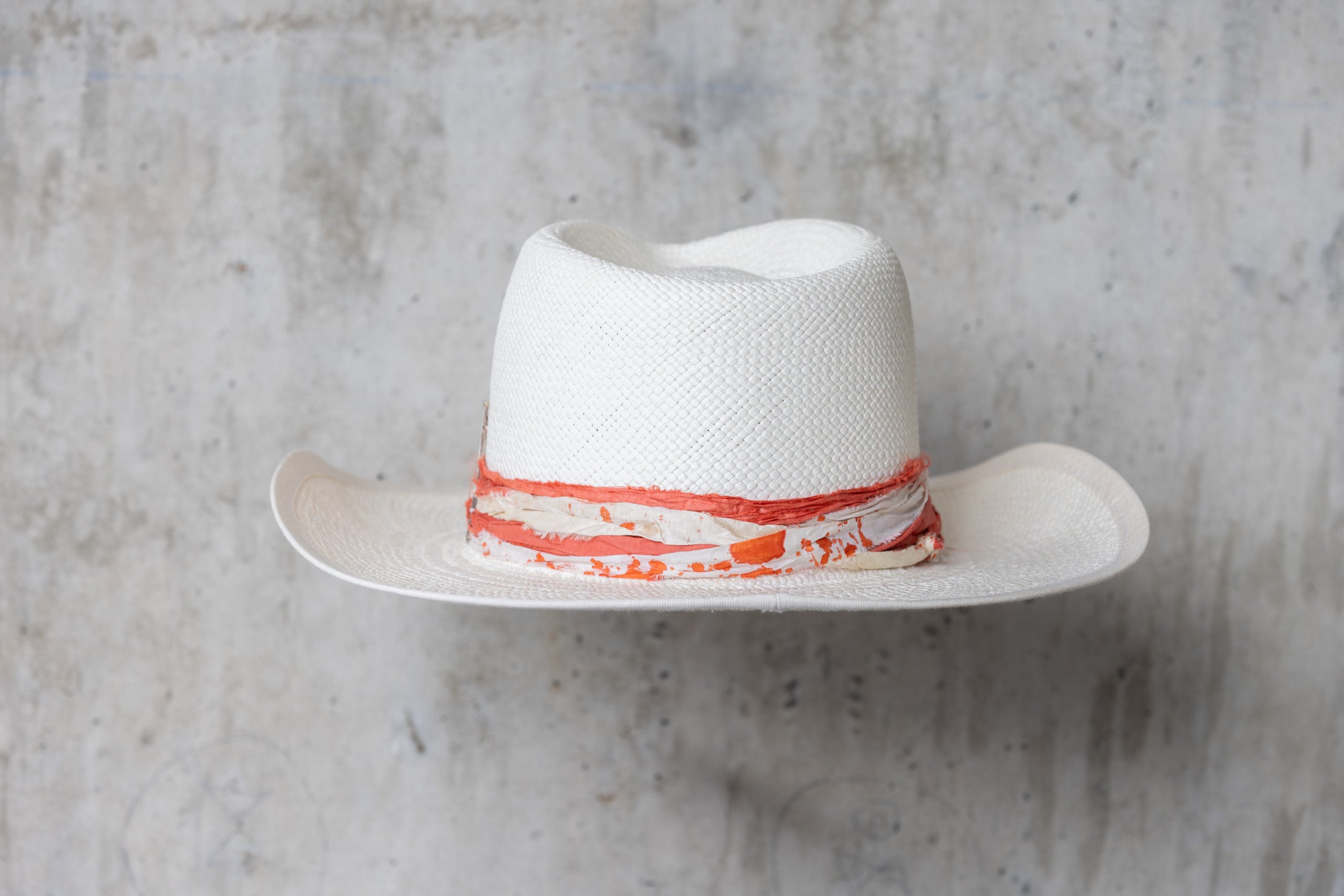 A white straw hat with an orange and cream band and a teardrop crown back