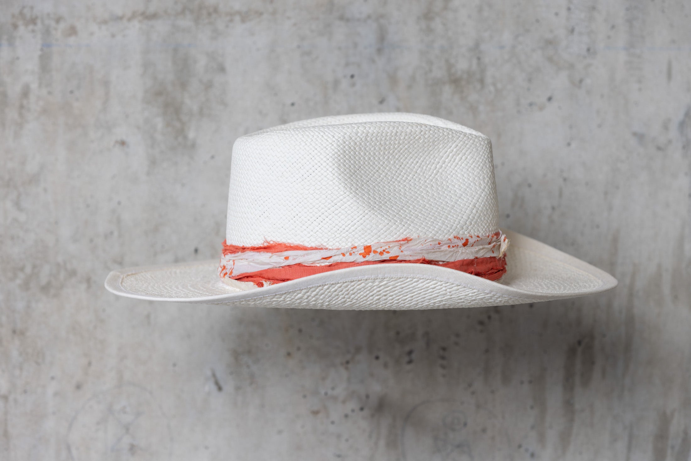 A white straw hat with an orange and cream band and a teardrop crown right side