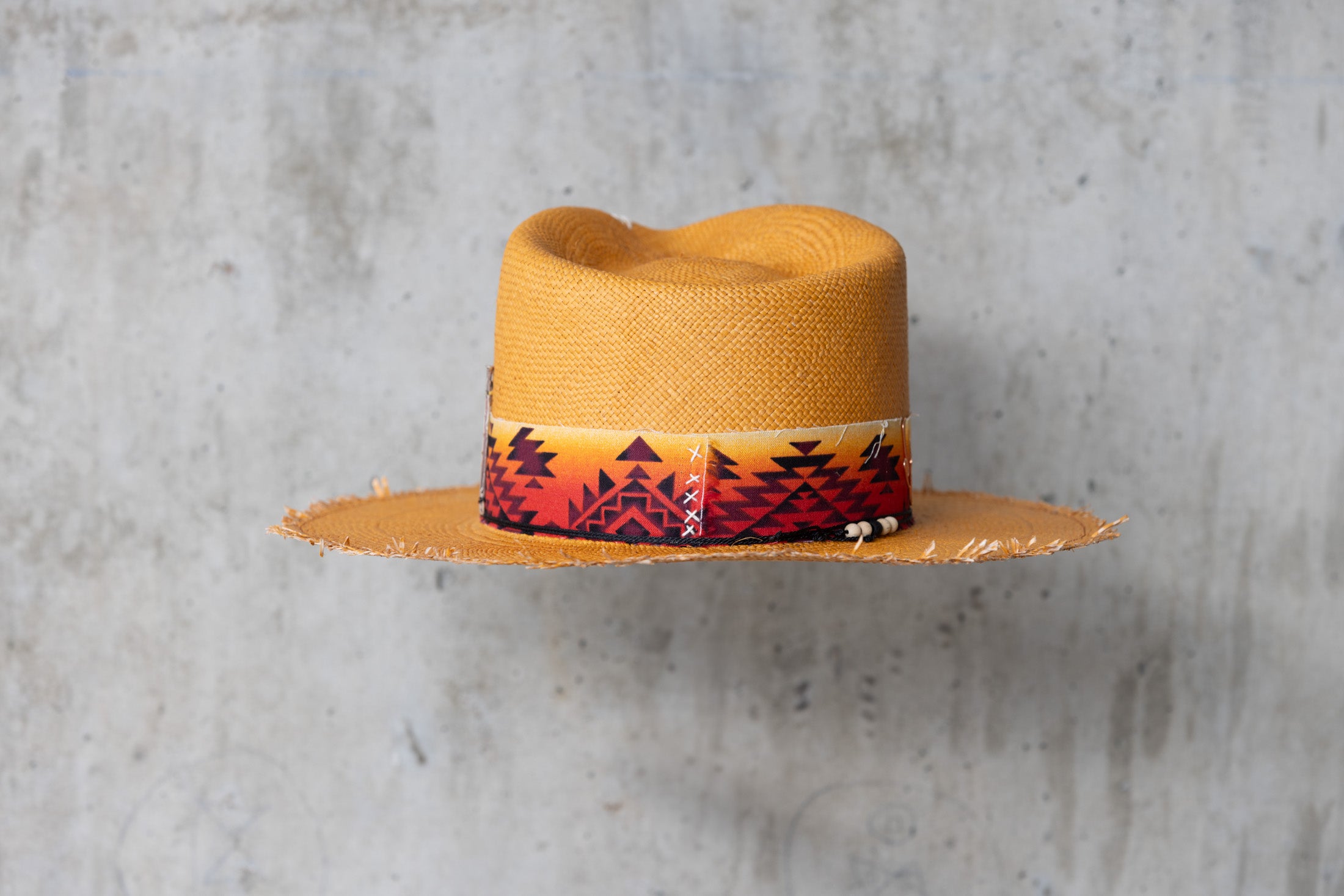 A Caramel colored straw hat with southwestern style band and frayed edge brim back