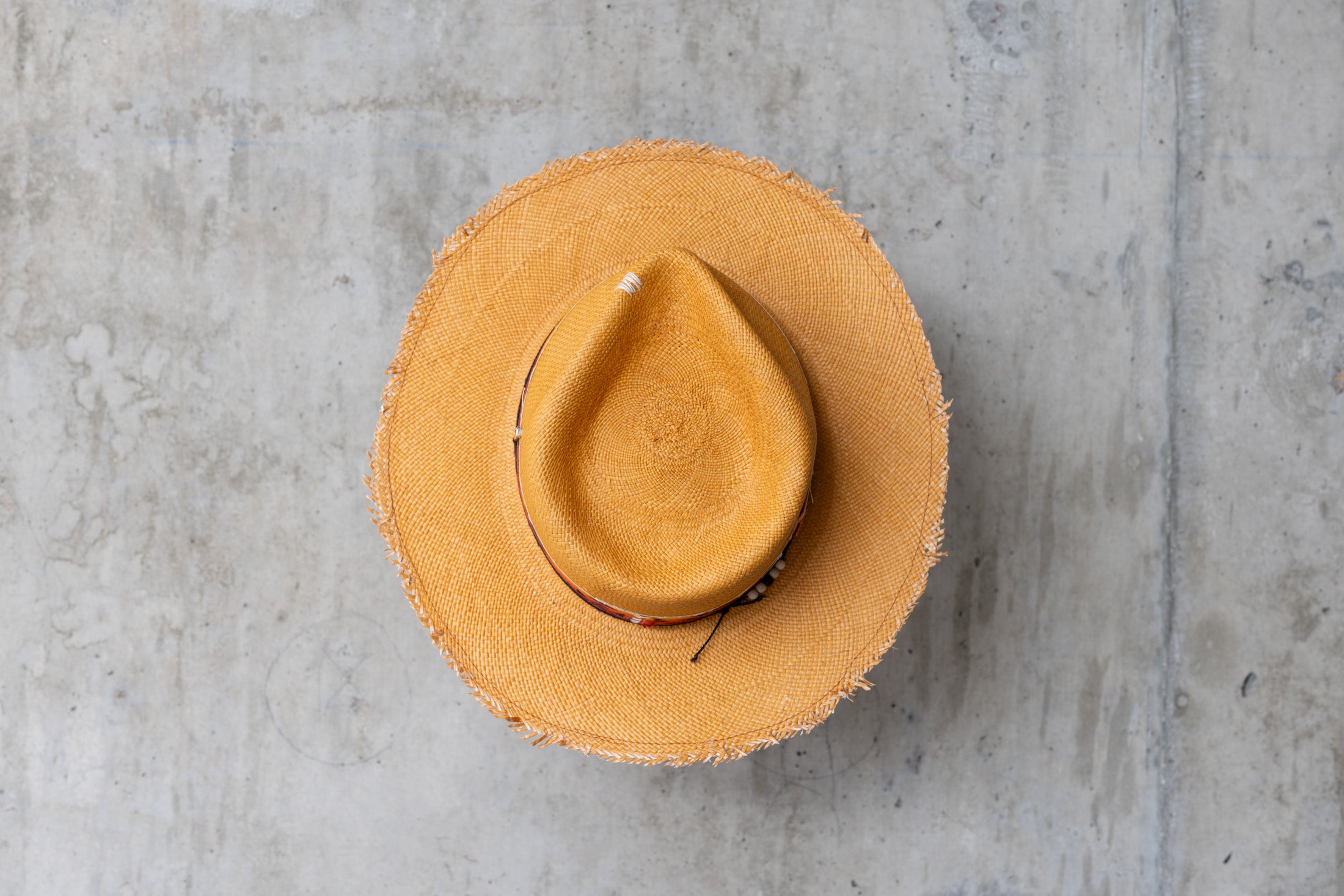A Caramel colored straw hat with southwestern style band and frayed edge brim top