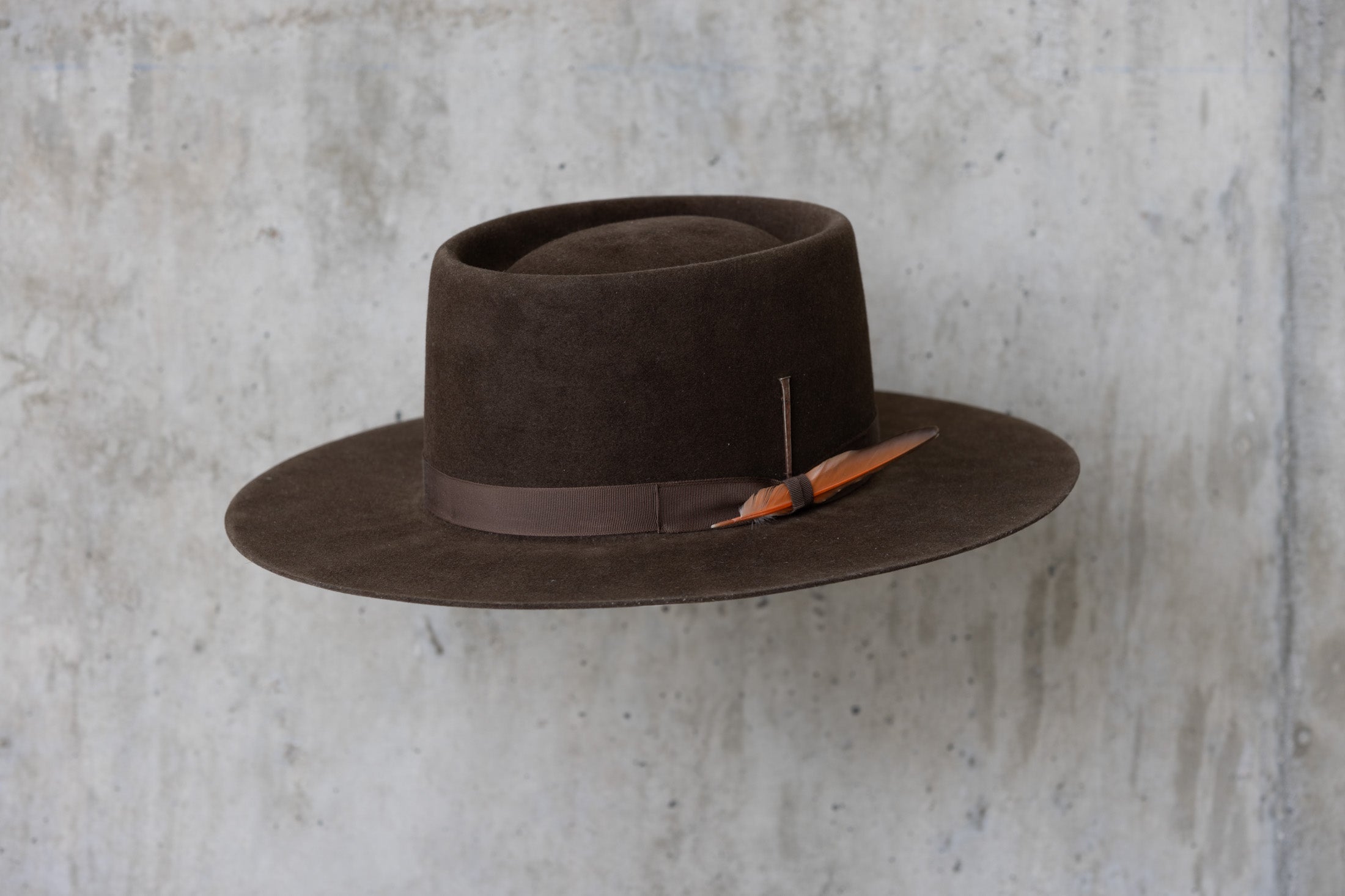 A dark brown felt Western cowboy hat with a telescope crown and a flat brim and feather for men and women left angle