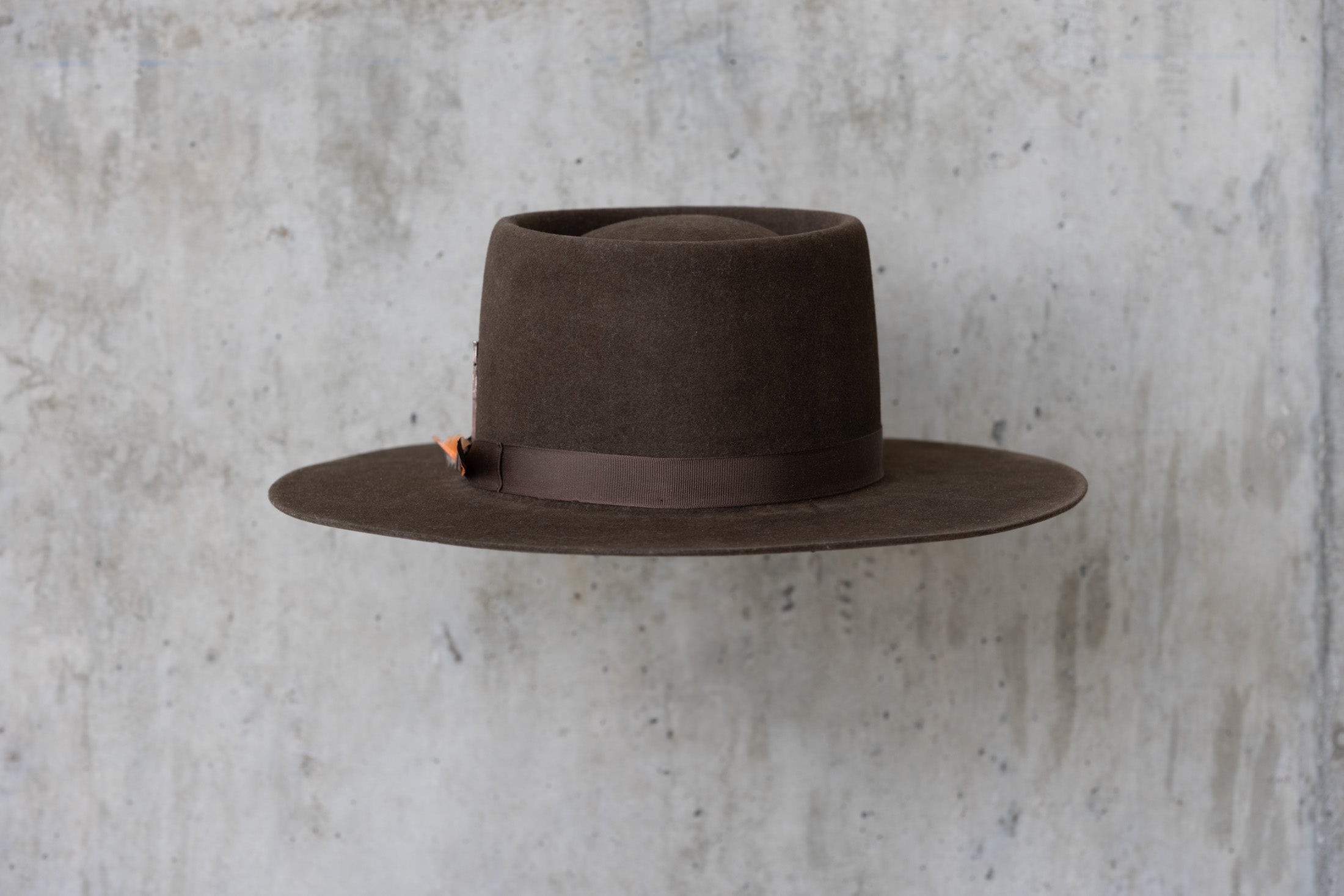 A dark brown felt Western cowboy hat with a telescope crown and a flat brim and feather for men and women front