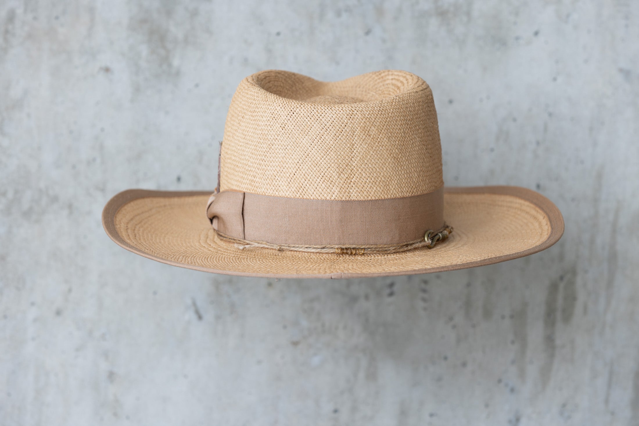 A beige straw cowboy hat in a toasty color with a teardrop crown and brown band back