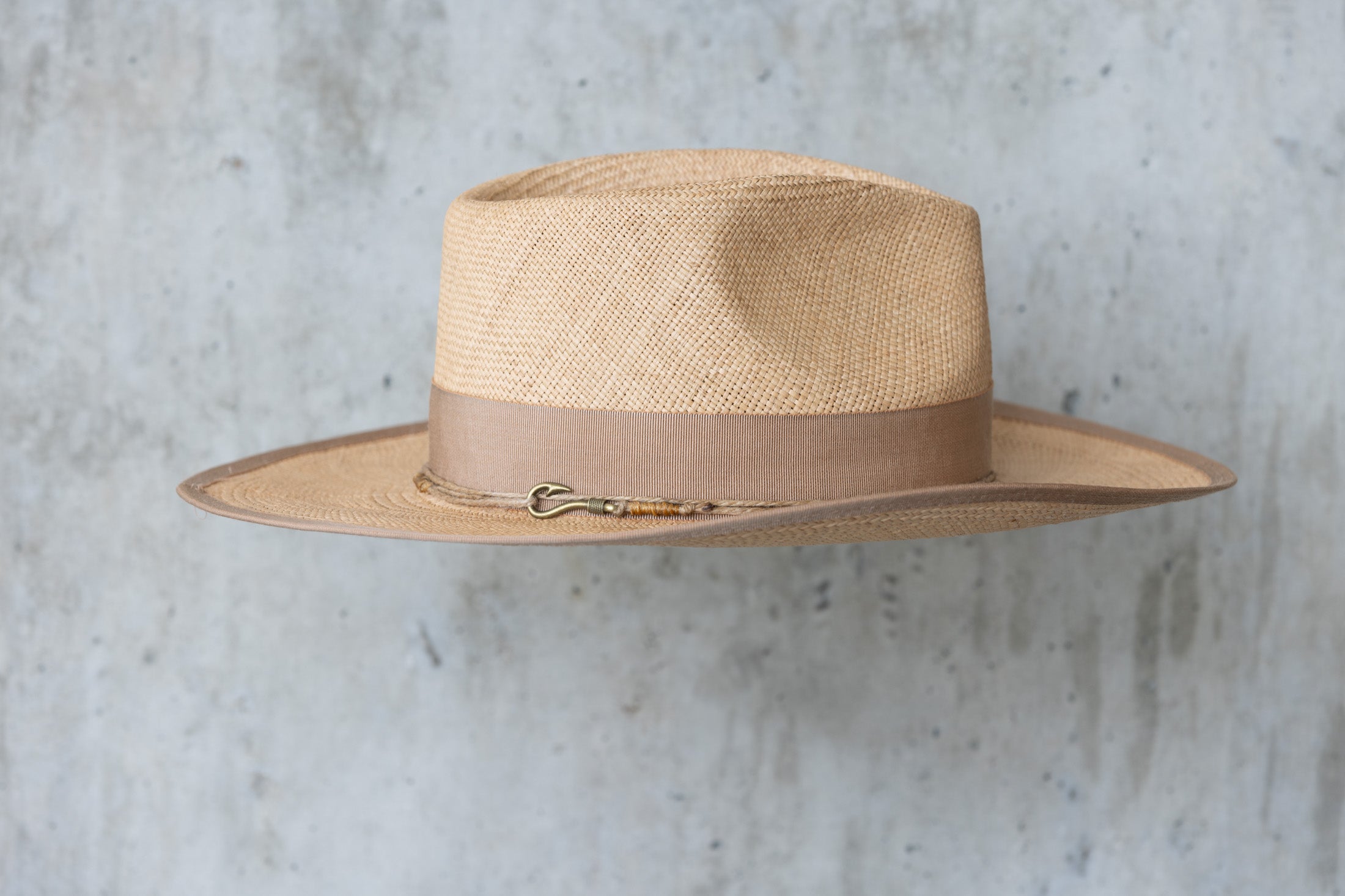 A beige straw cowboy hat in a toasty color with a teardrop crown and brown band right side