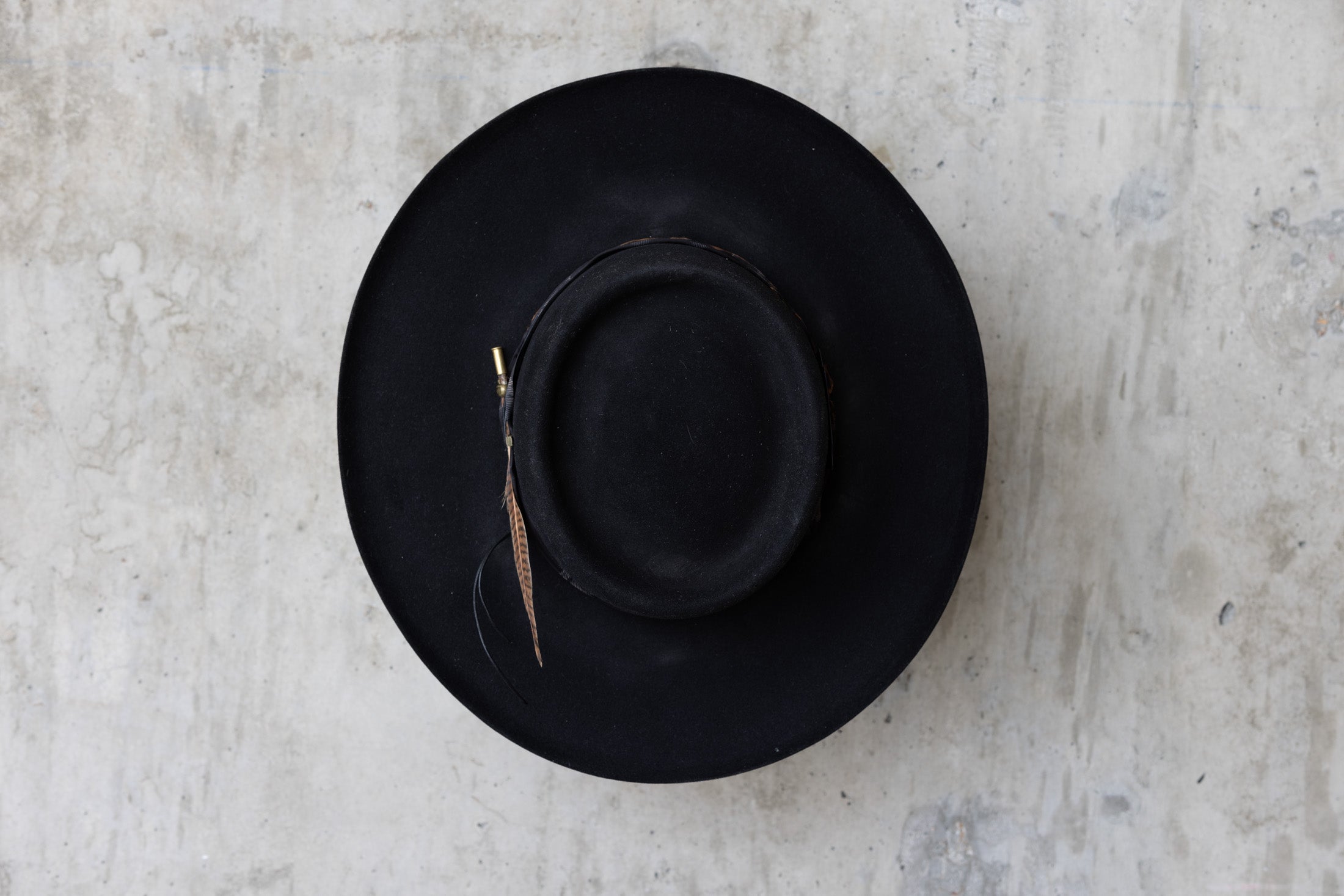 A black Western beaver felt cowboy hat with a wide brim telescope crown and a feather and leather band for men and women top