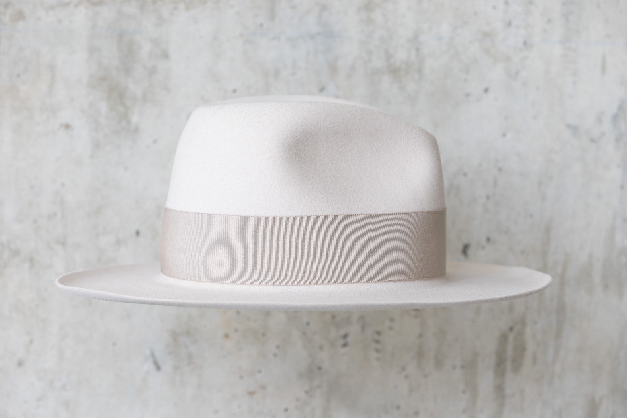 A beige-colored beaver felt hat with a bow and pencil curled brim edge right