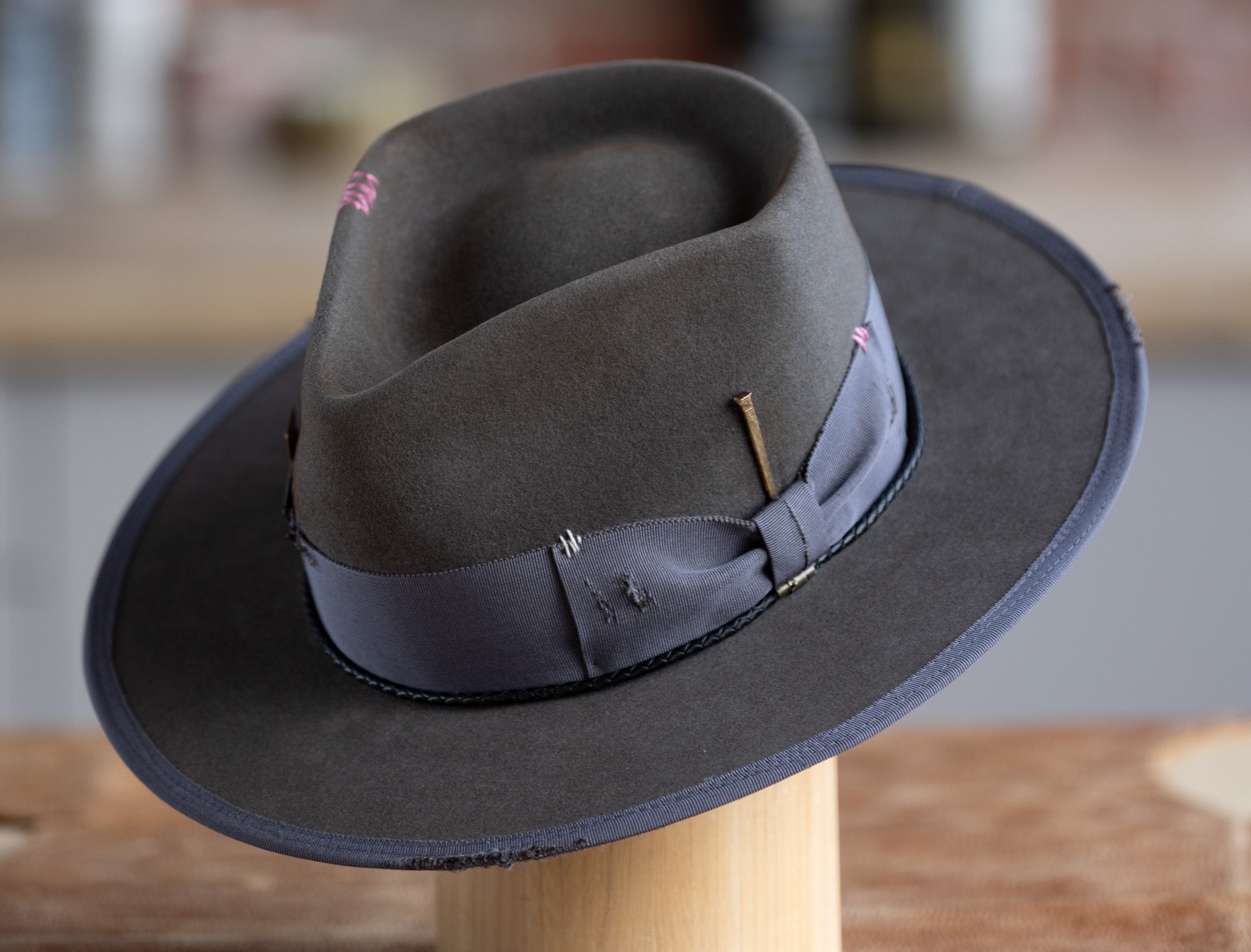 Gray fedora hat with a gray band on a wooden stand against a blurred background