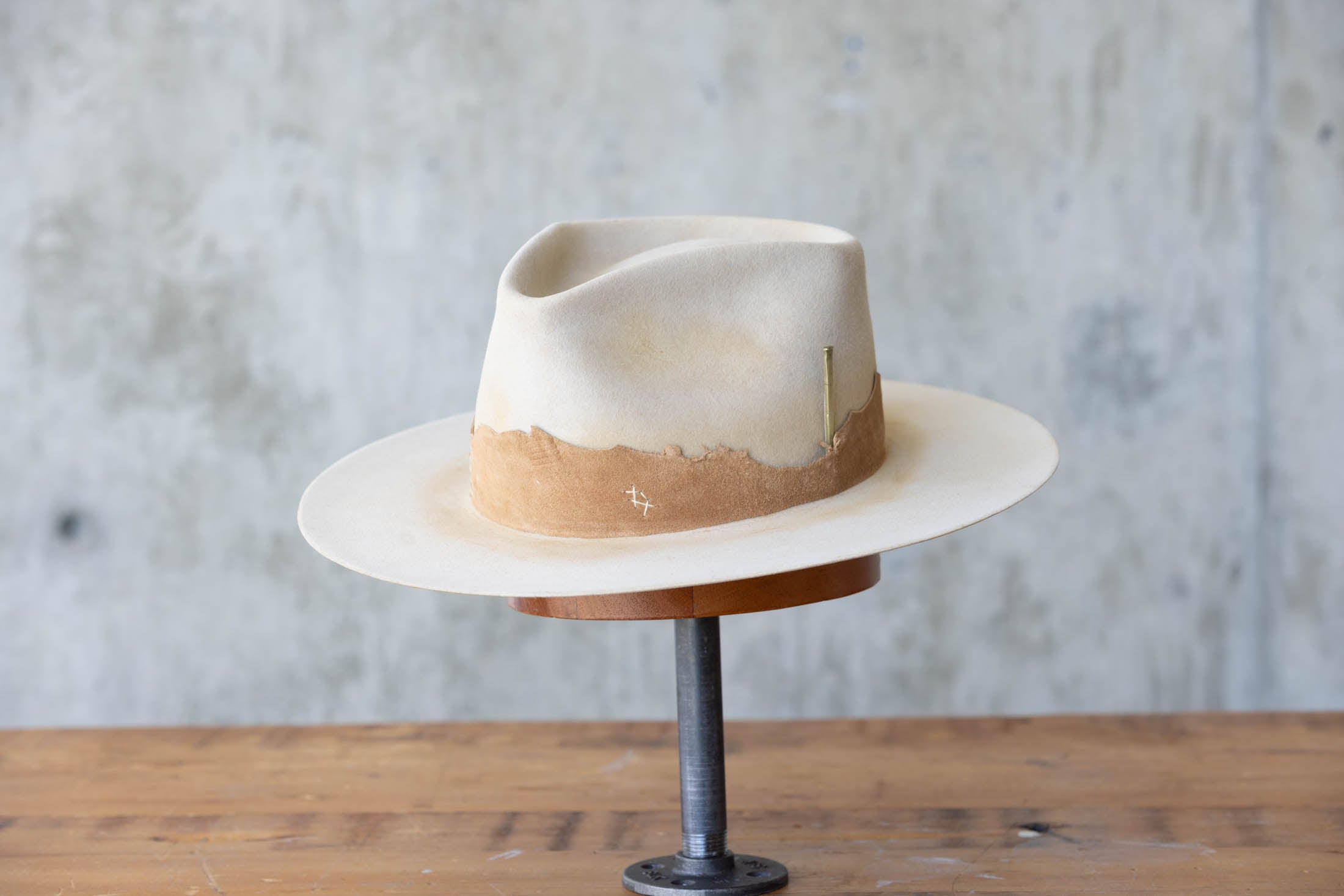 A beige Western hat with a teardrop crown  and brown leather band front angle
