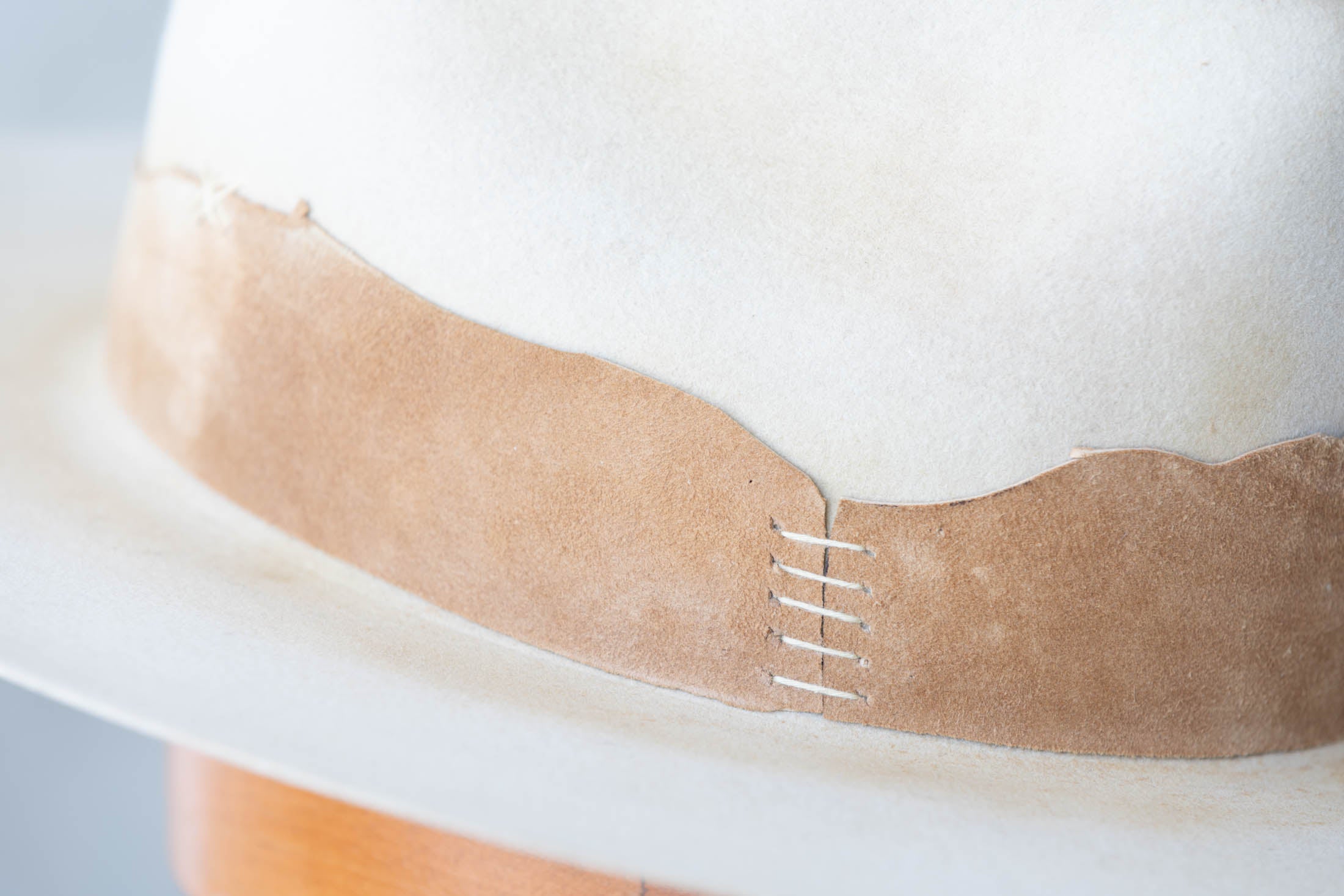 close up view of a beige hat with brown leather band and stitching