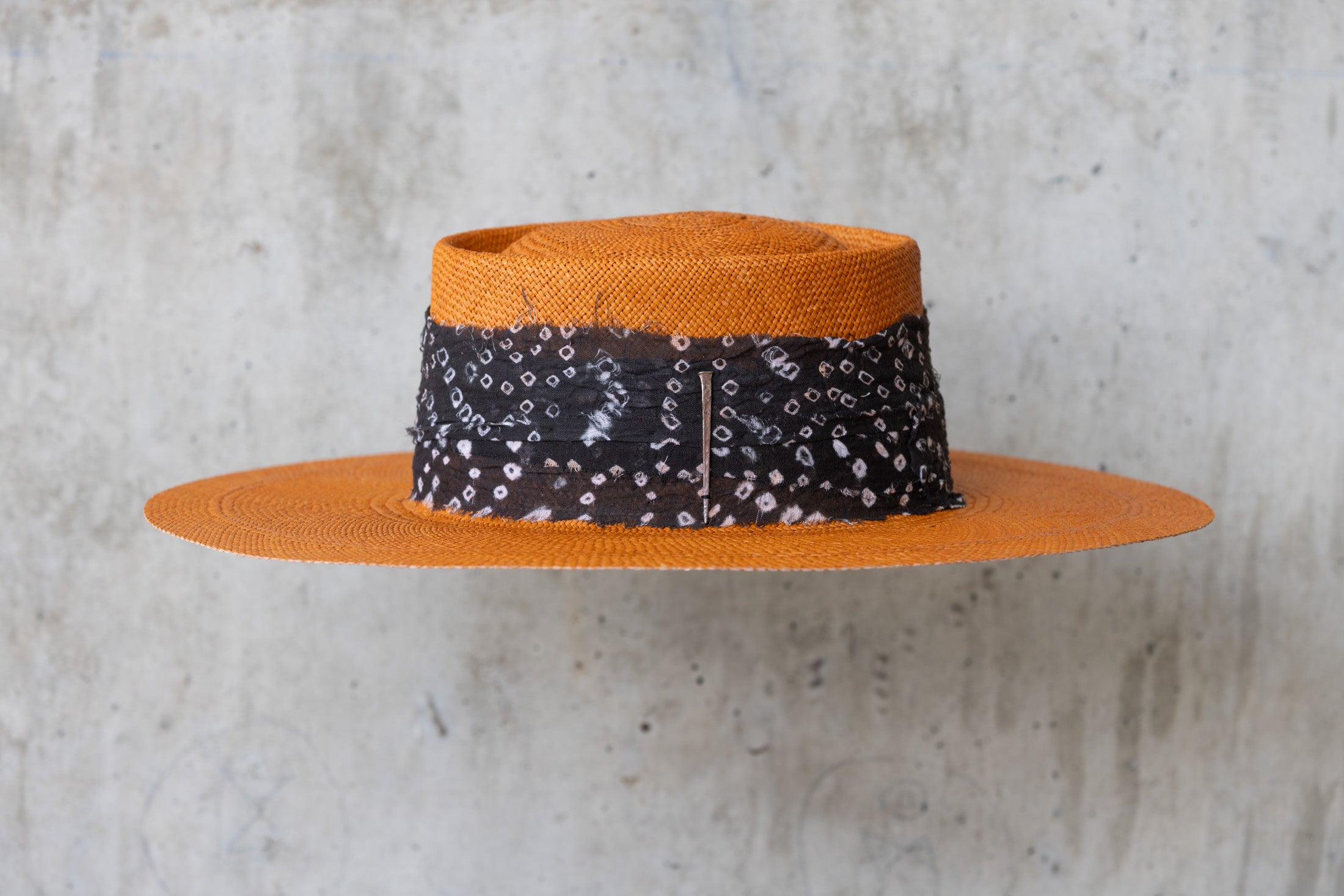 An orange straw hat with a black linen band with white print, featuring a telescope crown left side view