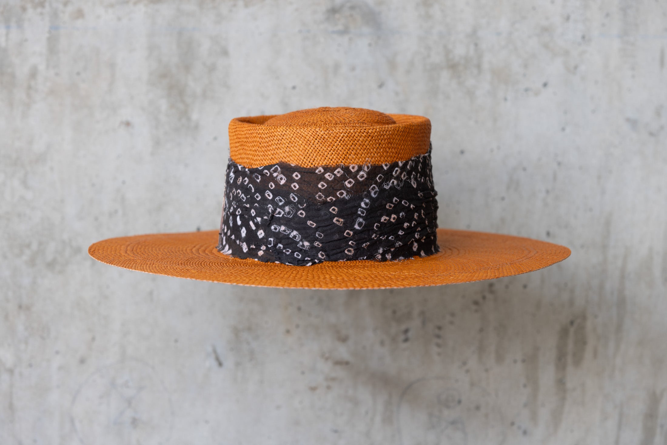An orange straw hat with a black linen band with white print, featuring a telescope crown back