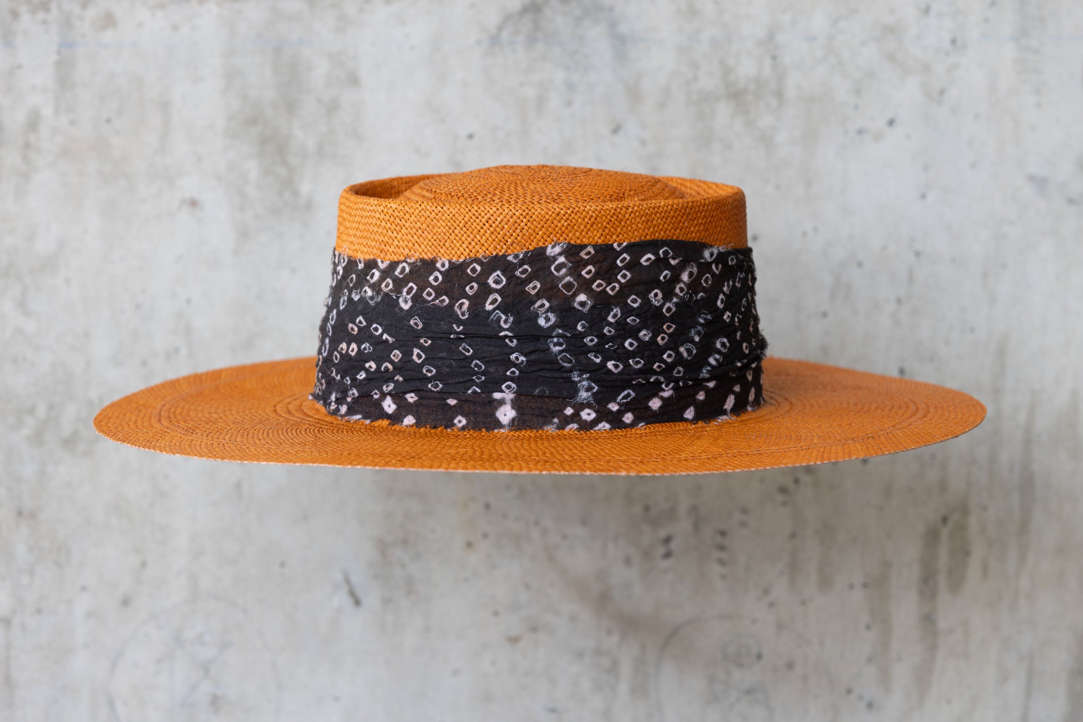 An orange straw hat with a black linen band with white print, featuring a telescope crown right side
