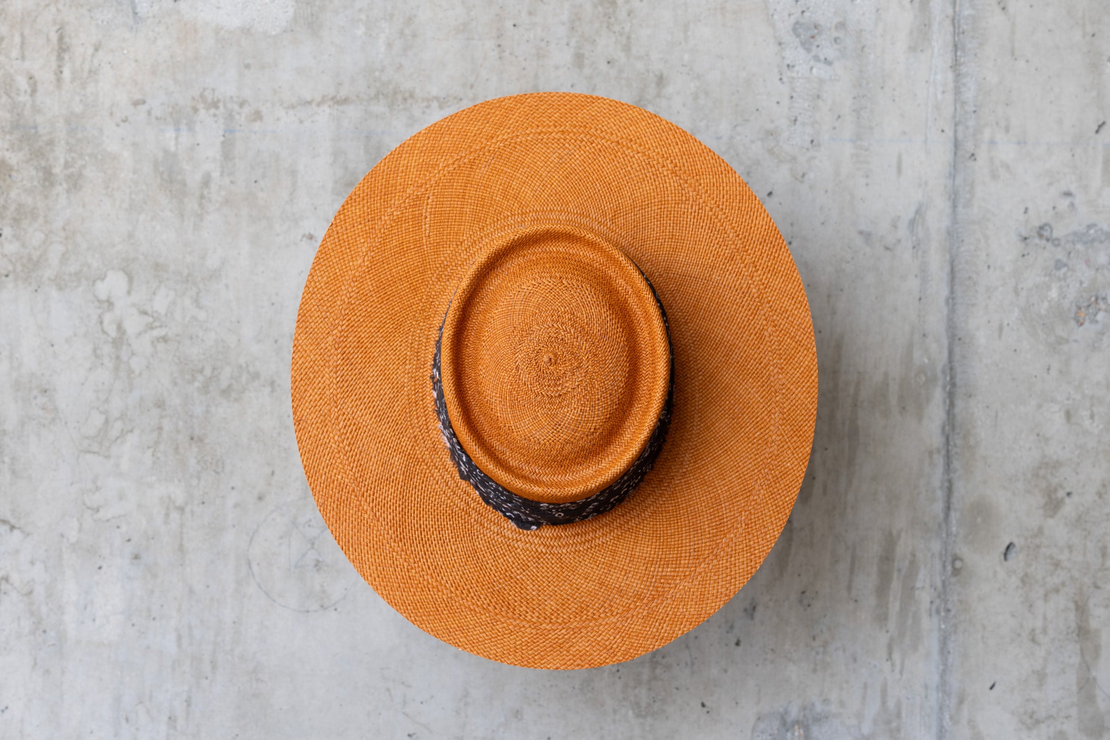 An orange straw hat with a black linen band with white print, featuring a telescope crown top