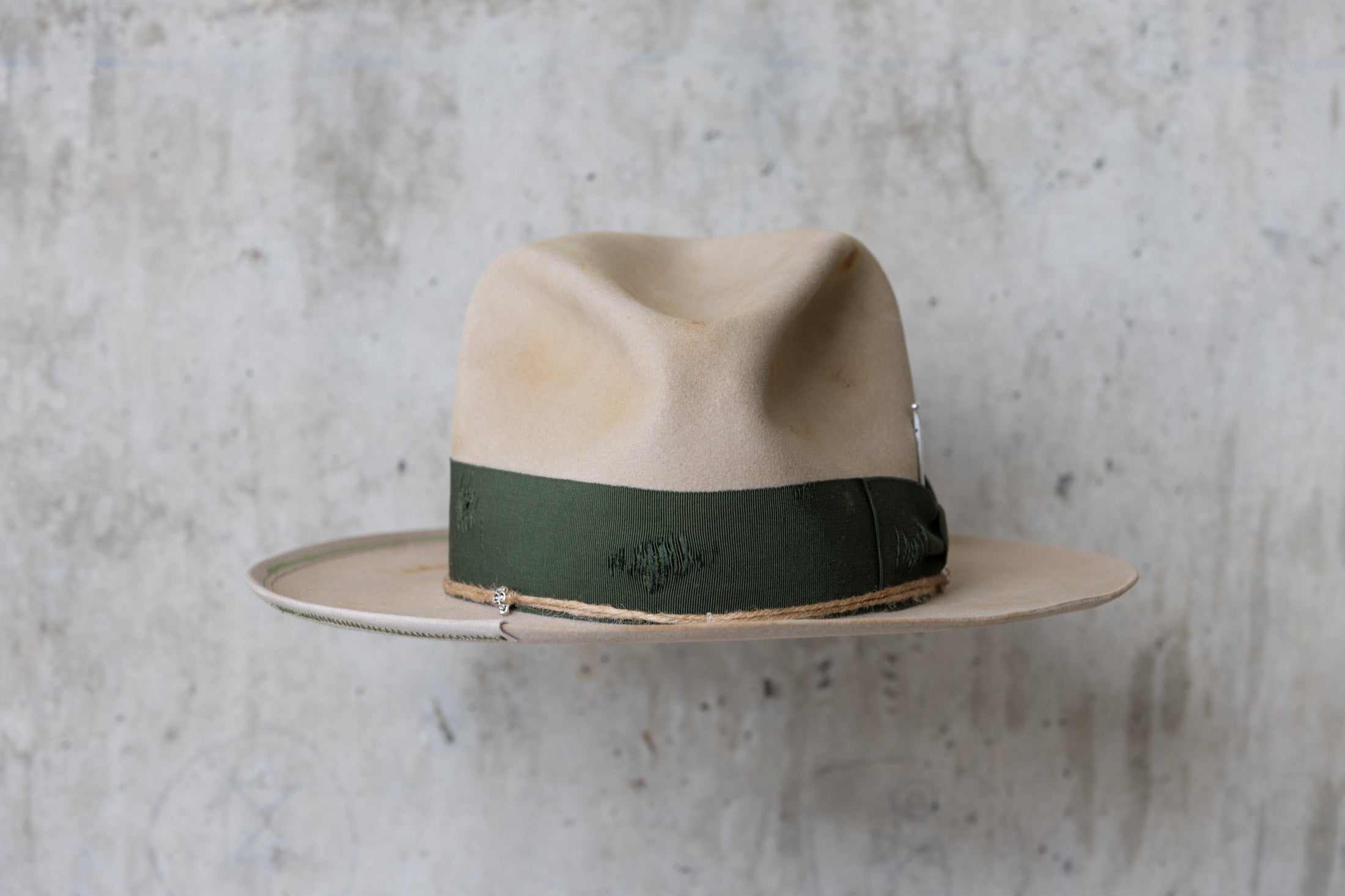 A beige cowboy hat with a forest green grosgrain band and a silver nail on the side front
