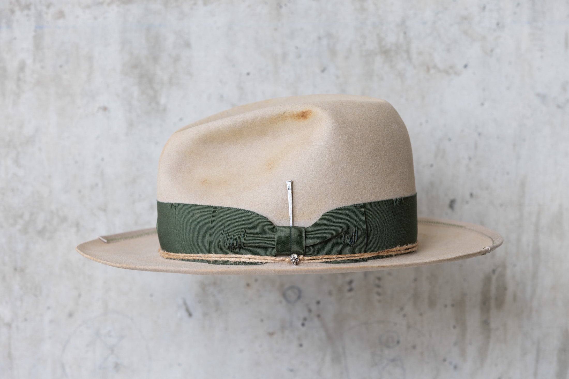 A beige cowboy hat with a forest green grosgrain band and a silver nail on the side left