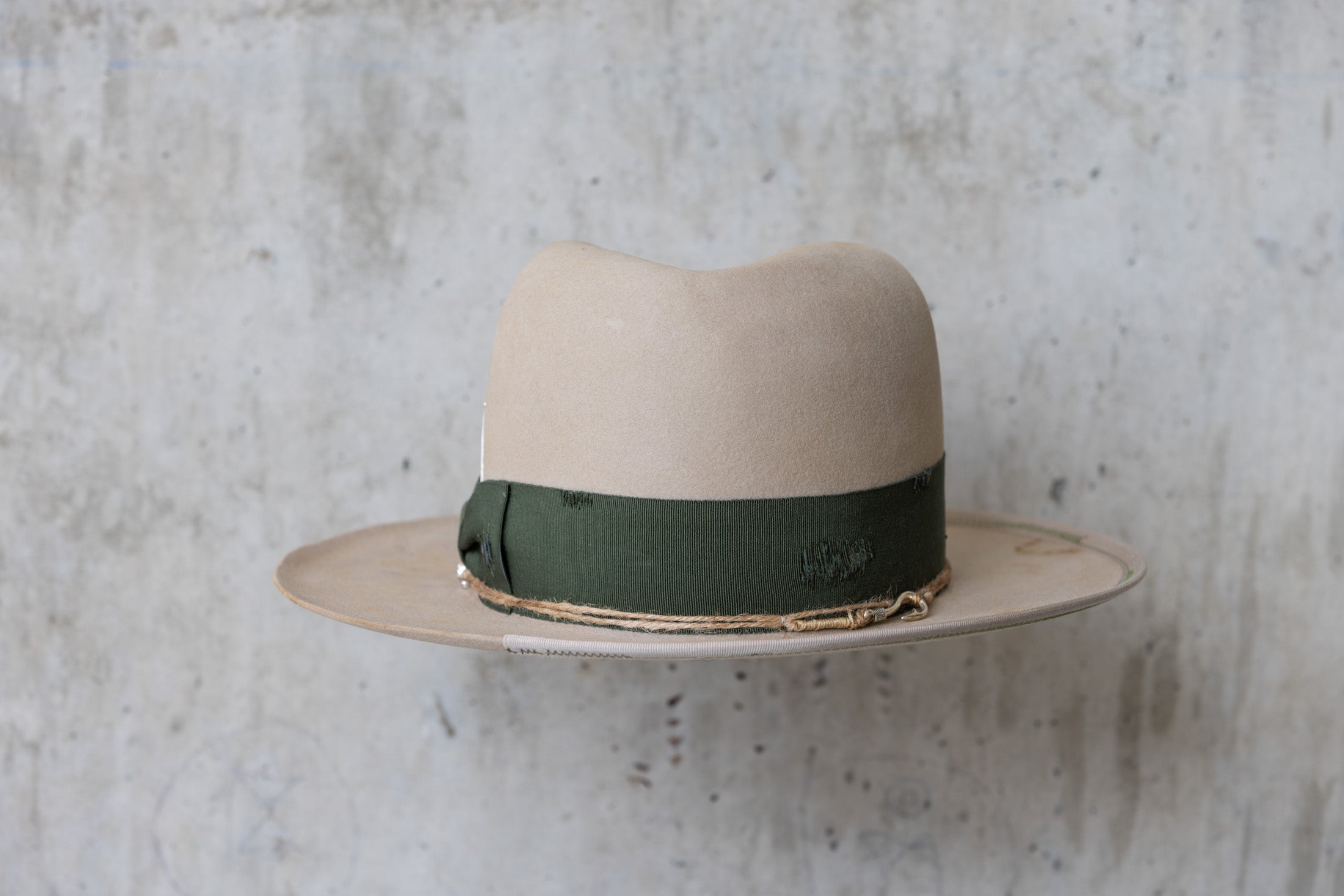 A beige cowboy hat with a forest green grosgrain band and a silver nail on the side back