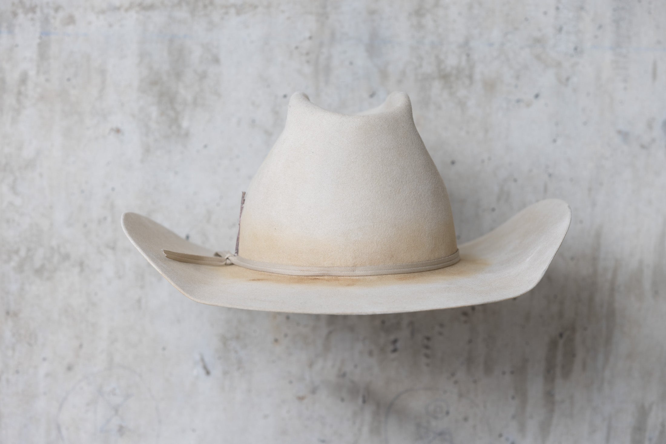 A beige, bone-colored cowboy hat with a mule kick and western flanged brim back side view