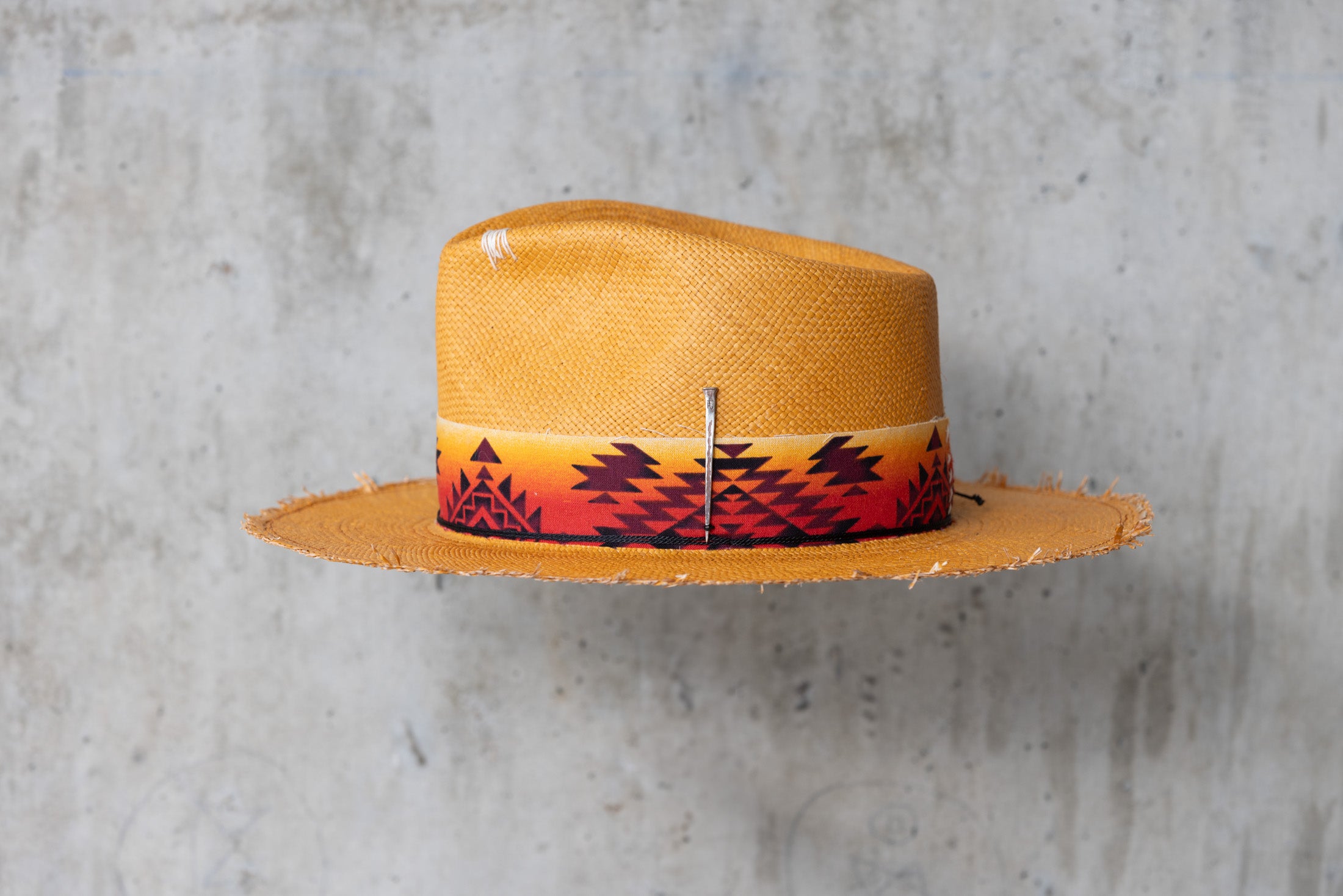 A Caramel colored straw hat with southwestern style band and frayed edge brim left side view 