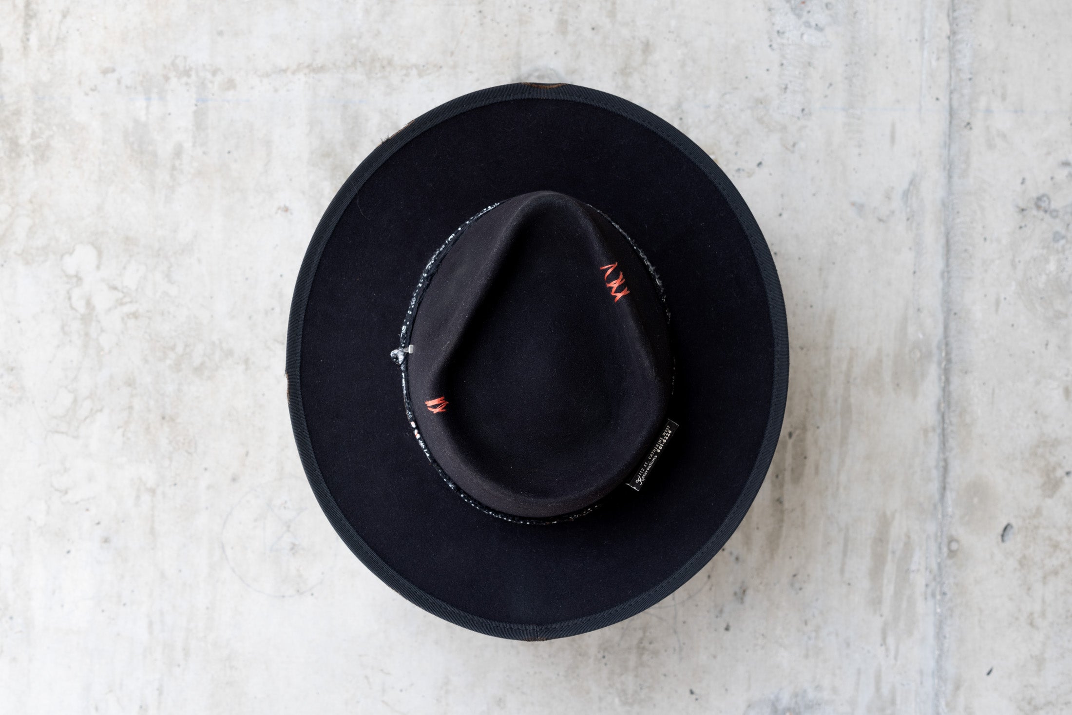 A black fedora western beaver felt hat with a teardrop crown and a brim featuring pencil curls. It has a black houndstooth band with a floral wrap and faded red stitching for men and women top