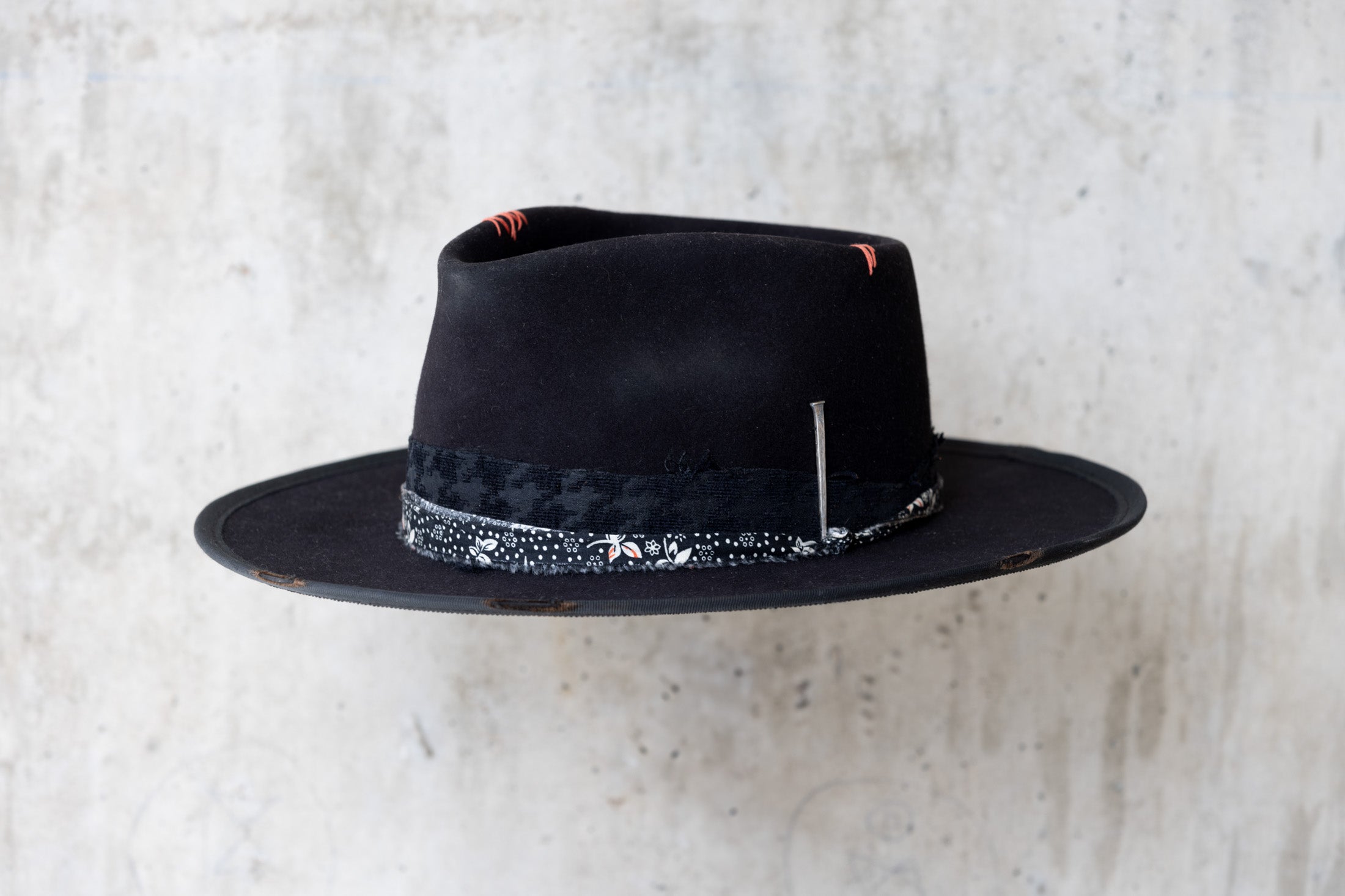 A black fedora western beaver felt hat with a teardrop crown and a brim featuring pencil curls. It has a black houndstooth band with a floral wrap and faded red stitching for men and women angle