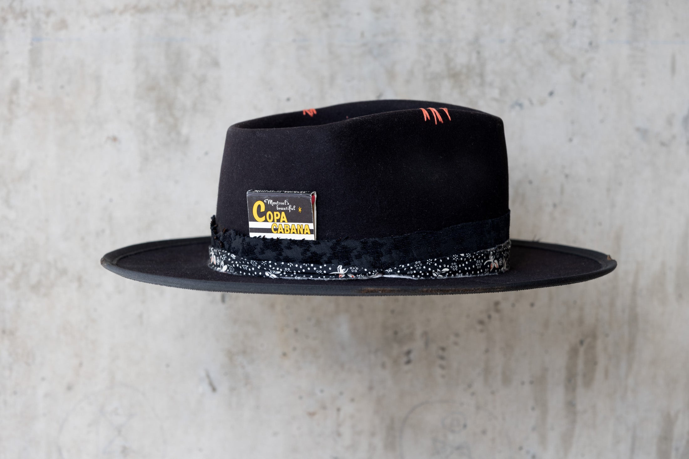 A black fedora western beaver felt hat with a teardrop crown and a brim featuring pencil curls. It has a black houndstooth band with a floral wrap and faded red stitching for men and women right