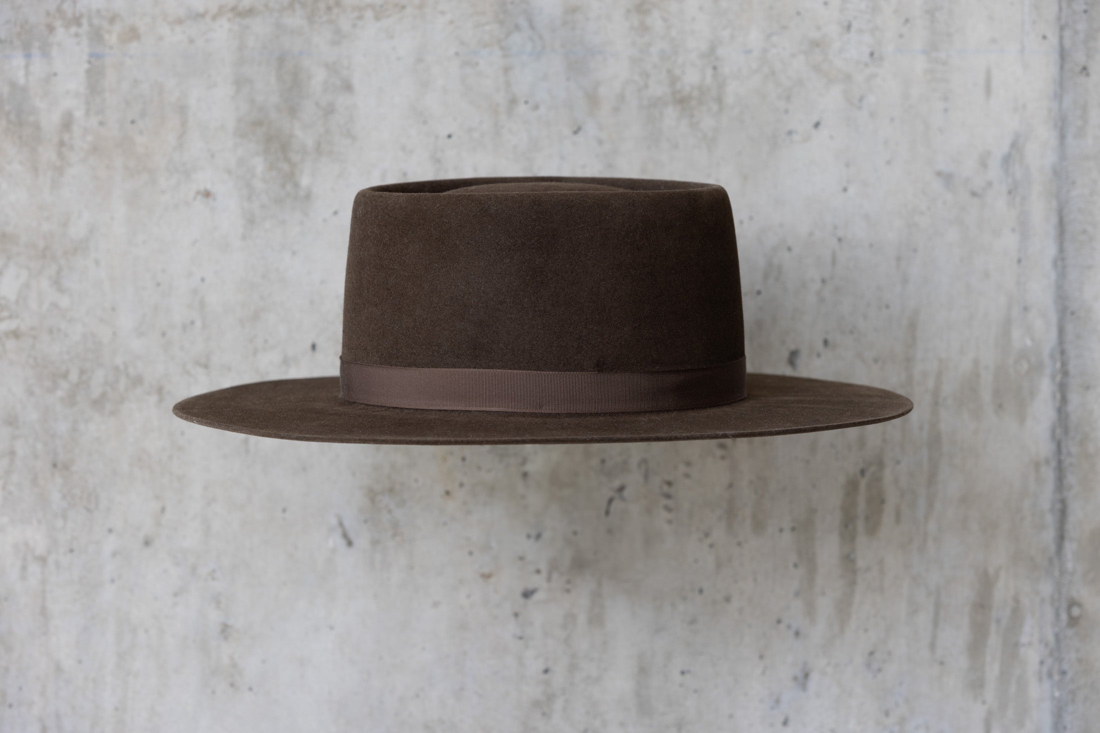 A dark brown felt Western cowboy hat with a telescope crown and a flat brim and feather for men and women right