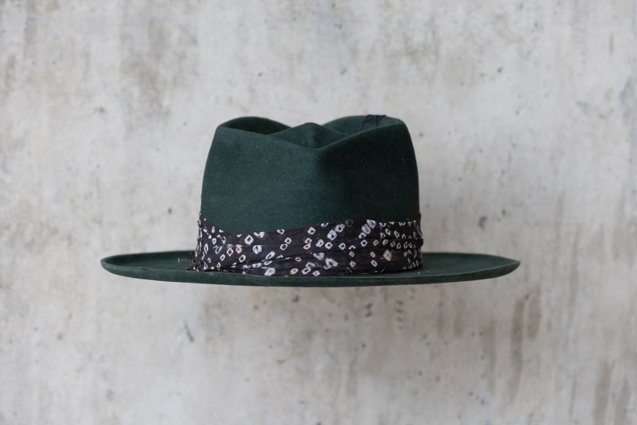 A forest green fedora-style felt hat with a black fabric band back