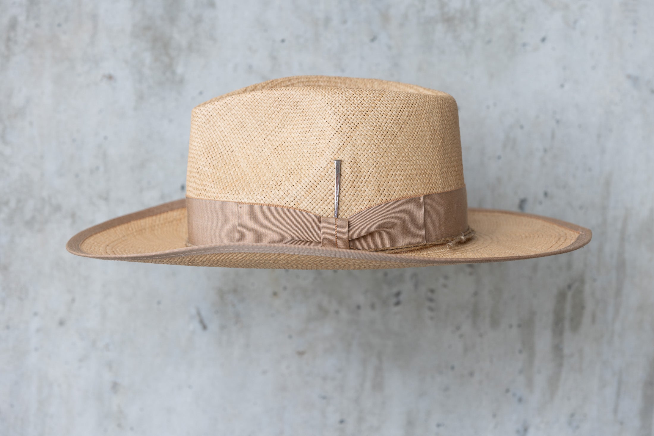 A beige straw cowboy hat in a toasty color with a teardrop crown and brown band left side