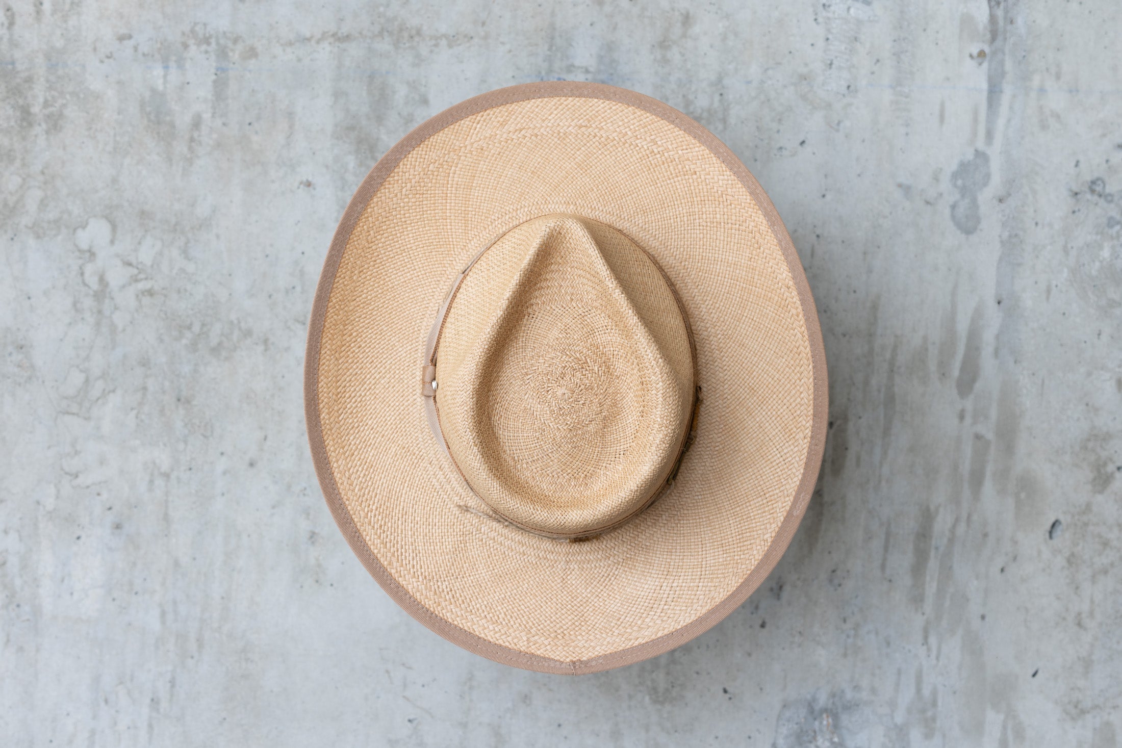 A beige straw cowboy hat in a toasty color with a teardrop crown and brown band top