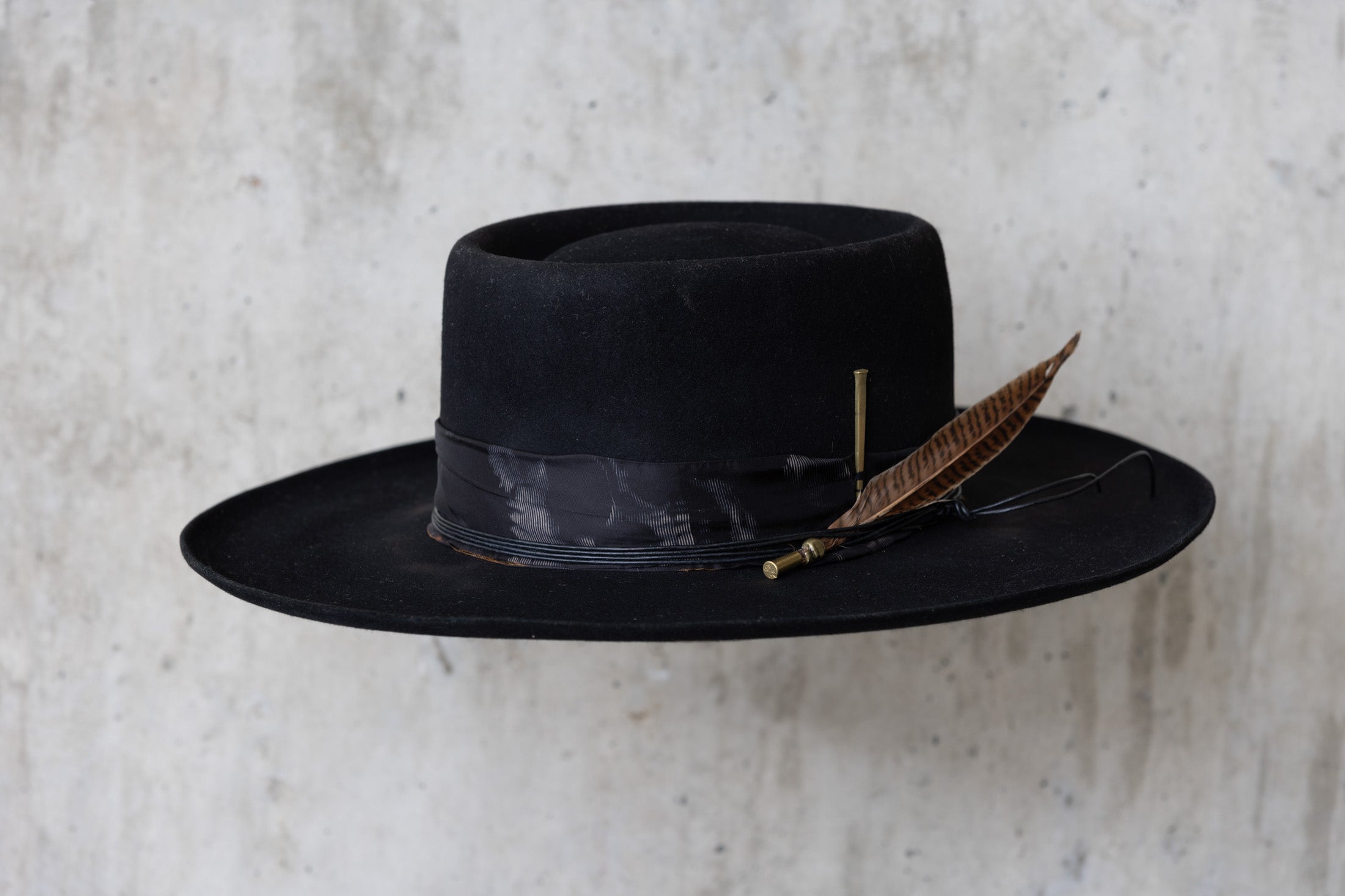 A black Western beaver felt cowboy hat with a wide brim telescope crown and a feather and leather band for men and women angle