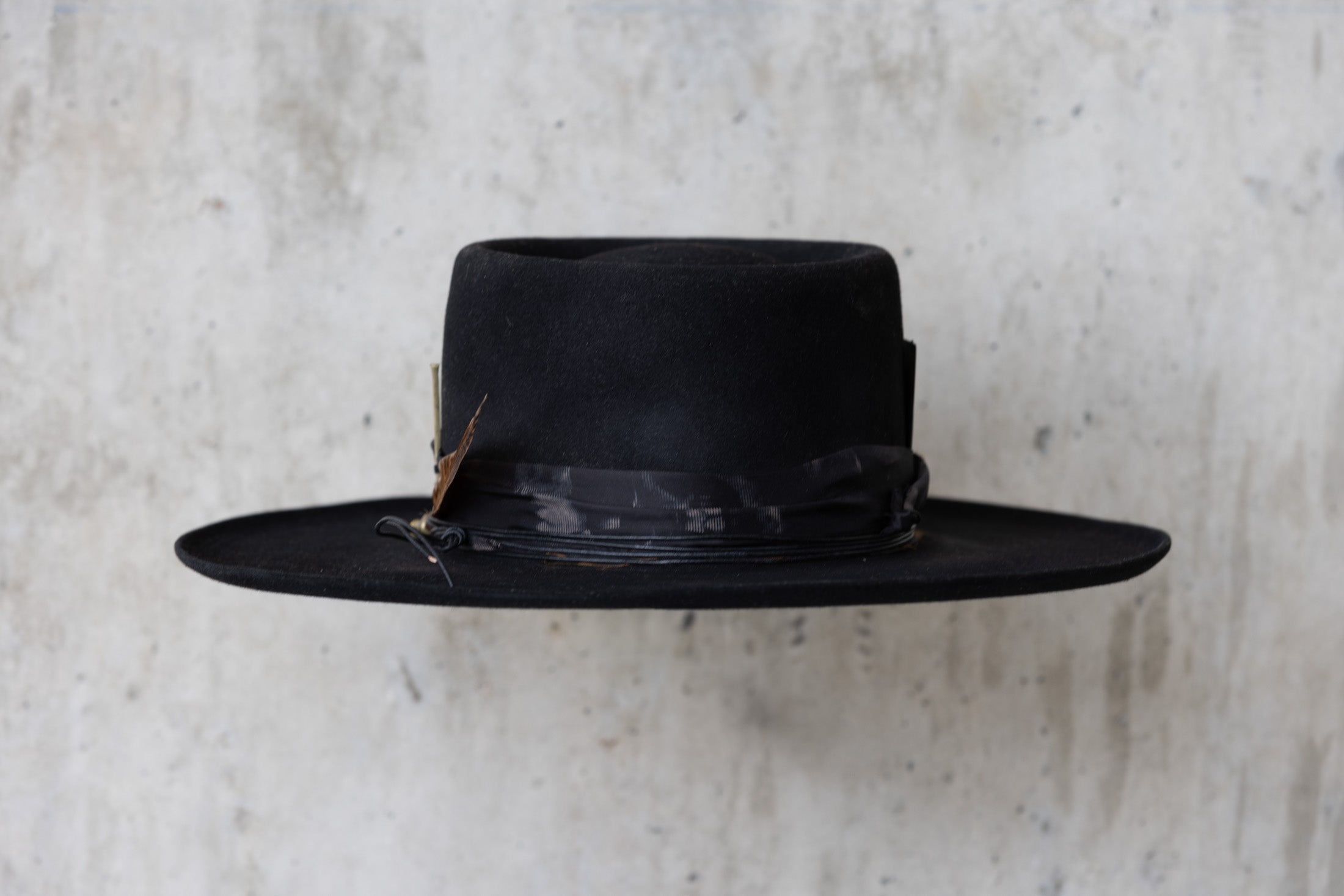 A black Western beaver felt cowboy hat with a wide brim telescope crown and a feather and leather band for men and women back