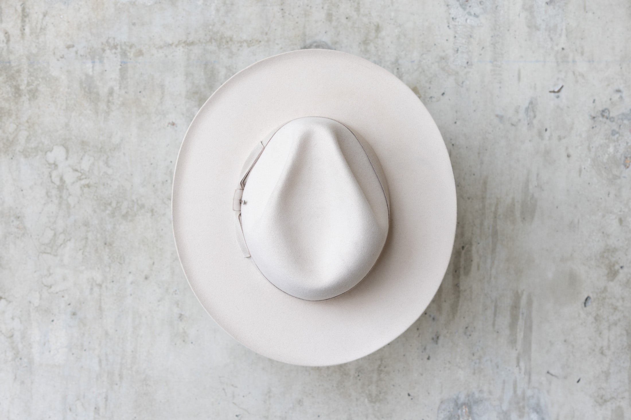 A beige-colored beaver felt hat with a bow and pencil curled brim edge top