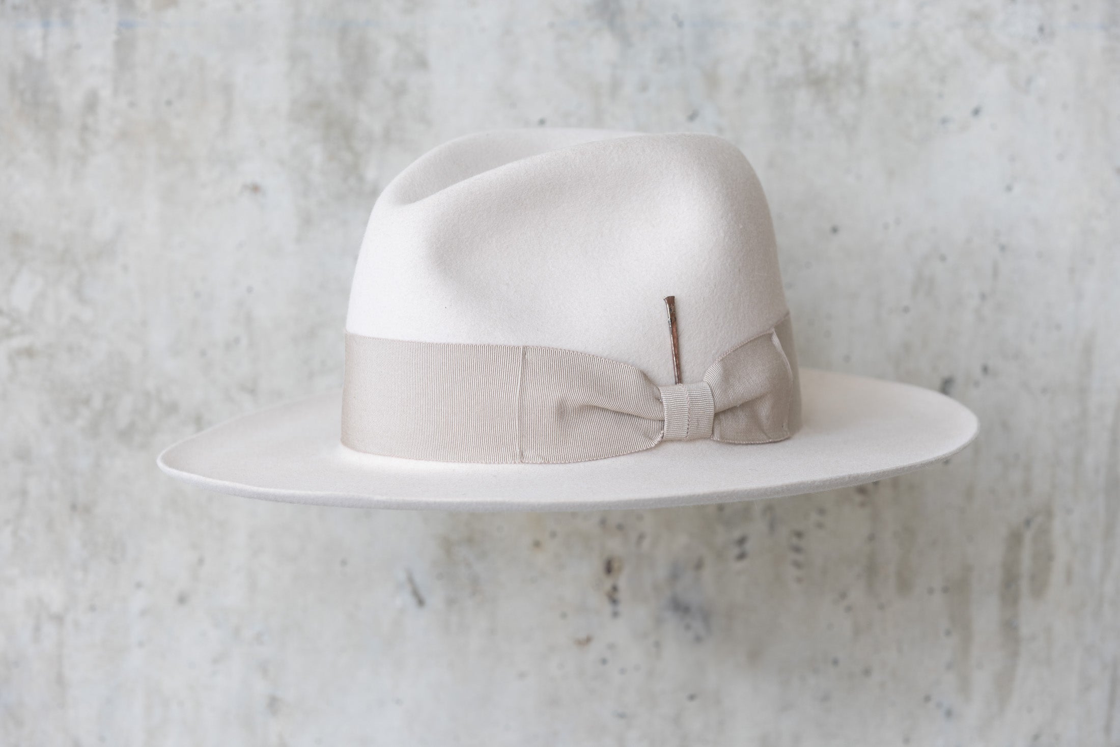 A beige-colored beaver felt hat with a bow and pencil curled brim edge angle view