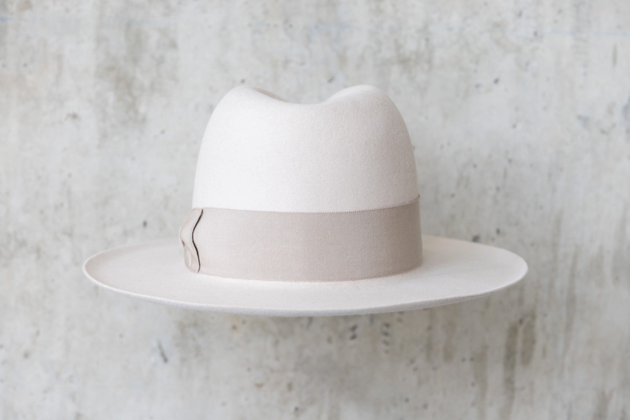 A beige-colored beaver felt hat with a bow and pencil curled brim edge back