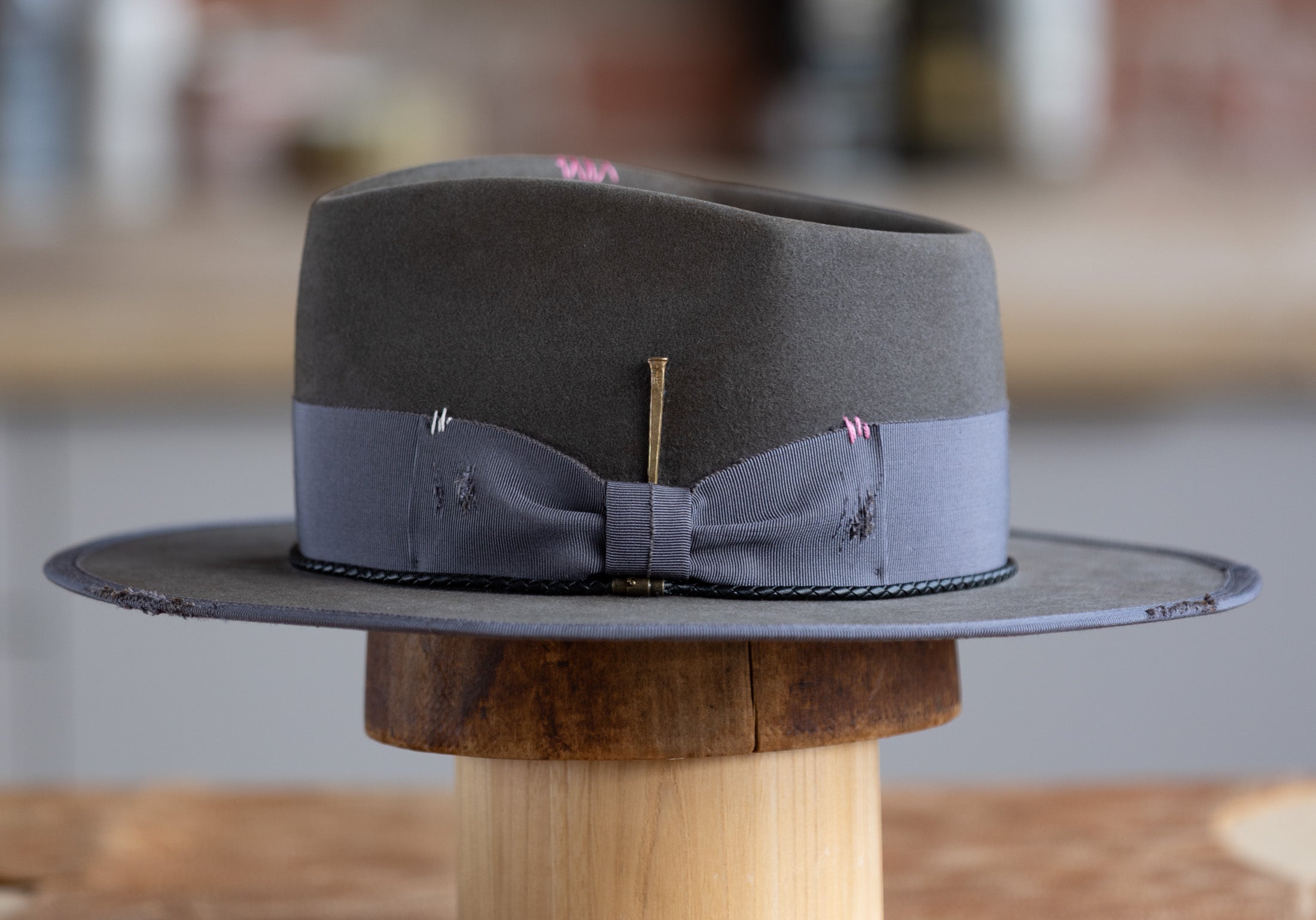 Gray fedora hat with a bow tie on a wooden stand against a blurred background