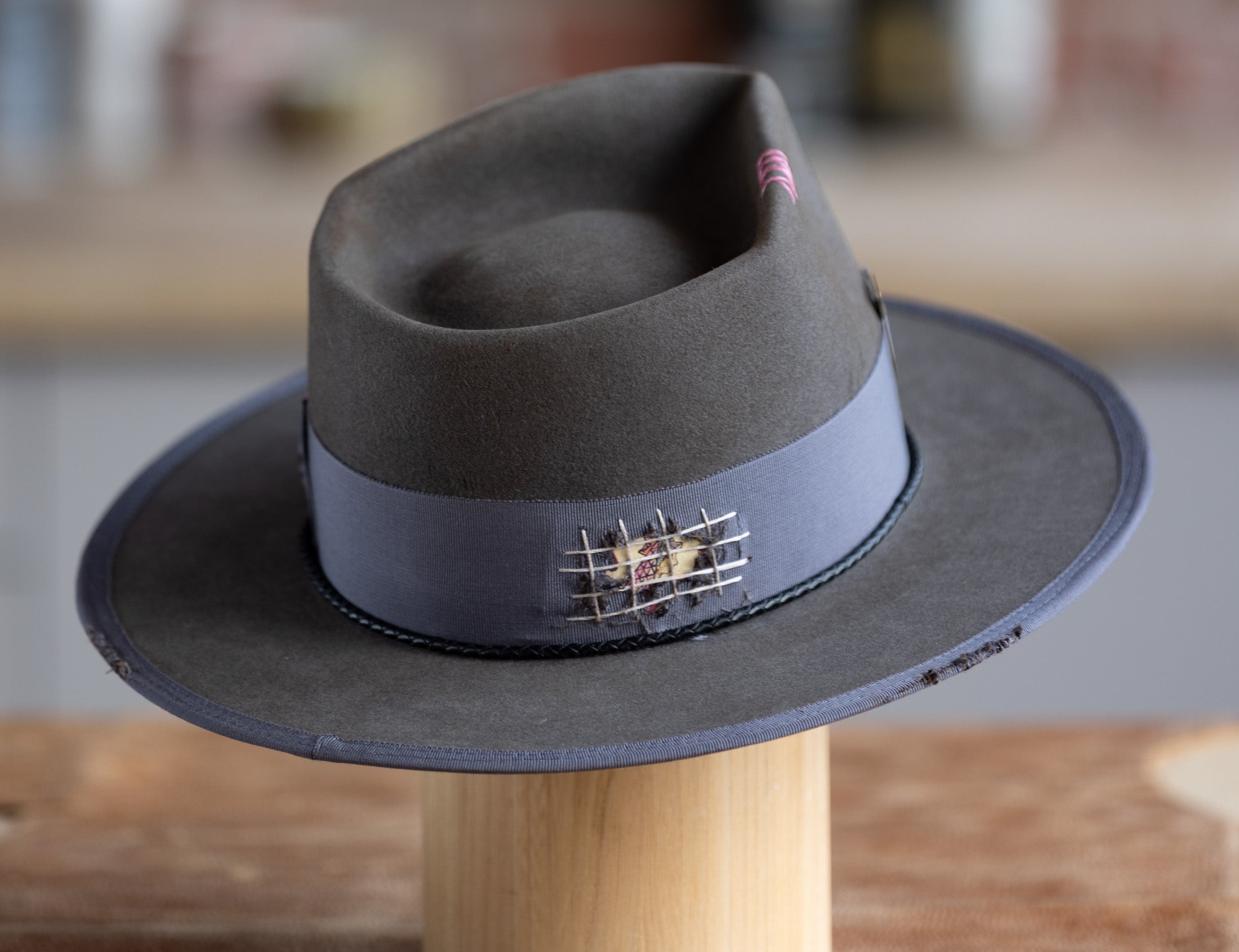 Gray fedora hat with a decorative band on a wooden stand